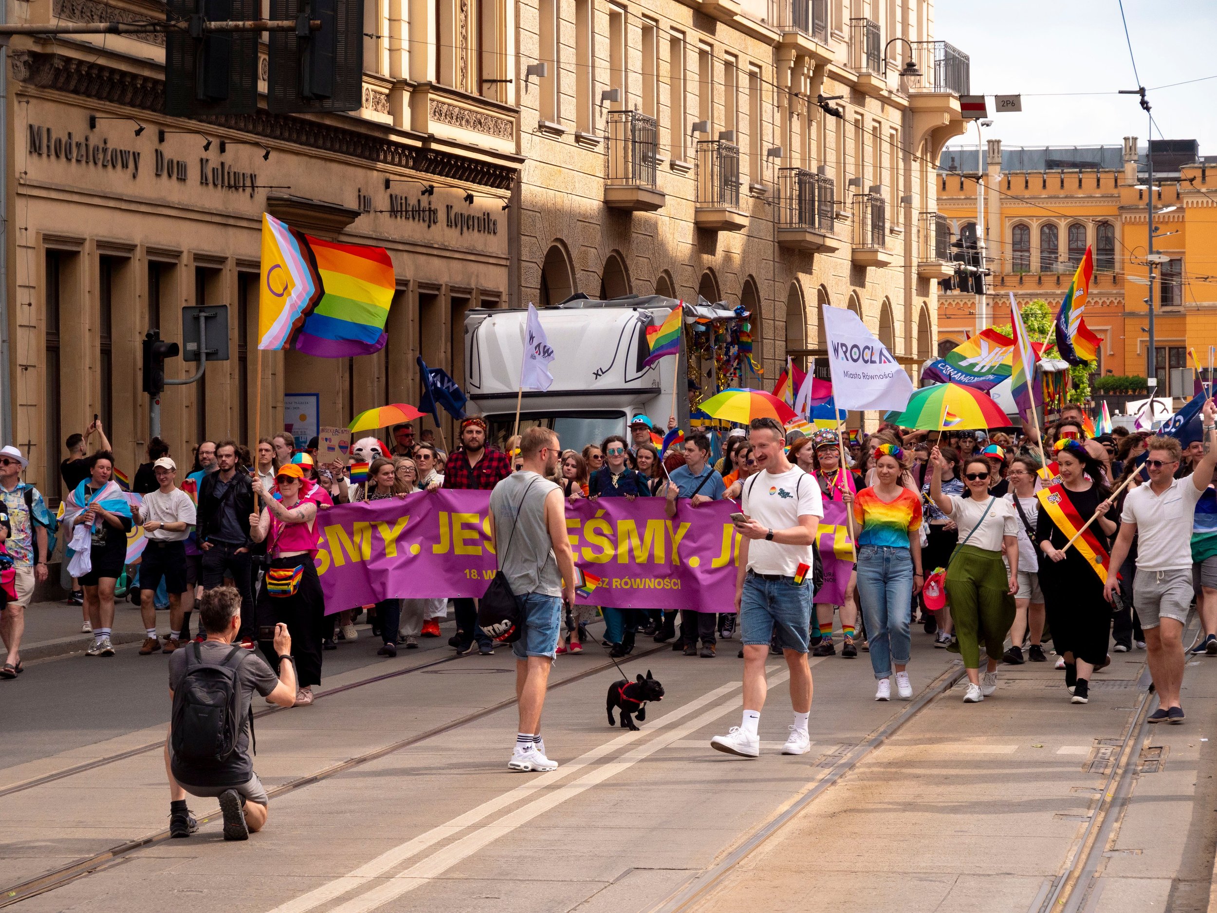 Crowd taking part in a Pride parade with rainbow flags and banners, representing LGBTQ+ visibility, inclusion, belonging and the importance of safer, more welcoming public spaces during Pride Month.