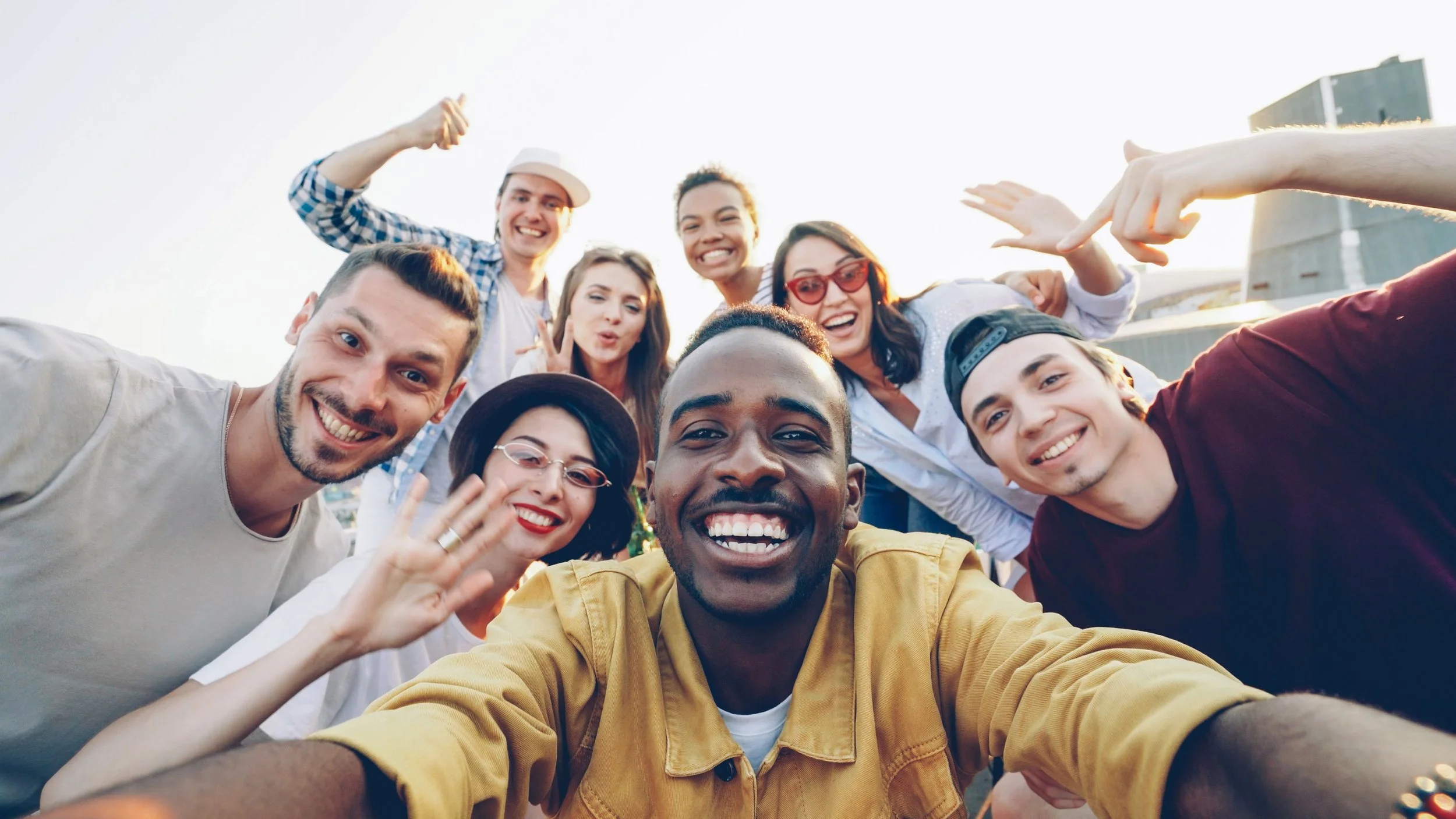 Diverse group of young adults smiling together outdoors, representing friendship, belonging, inclusion and the power of community connection during Month of Community.