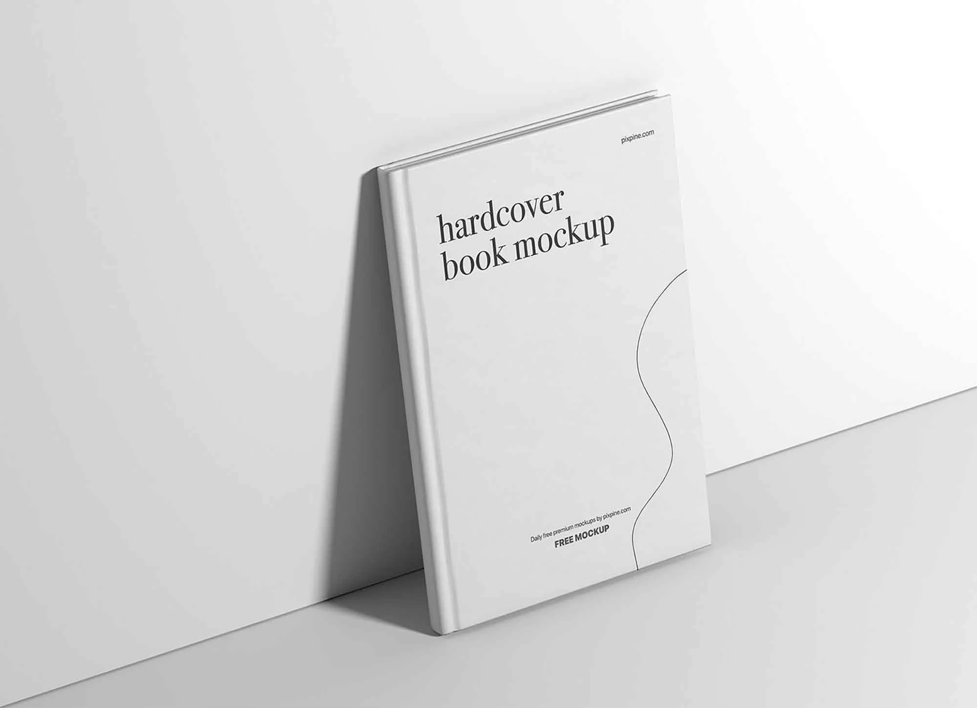 A white hardcover book mockup with the text 'hardcover book mockup' on the cover, leaning against a white wall with a white envelope or sheet beside it.