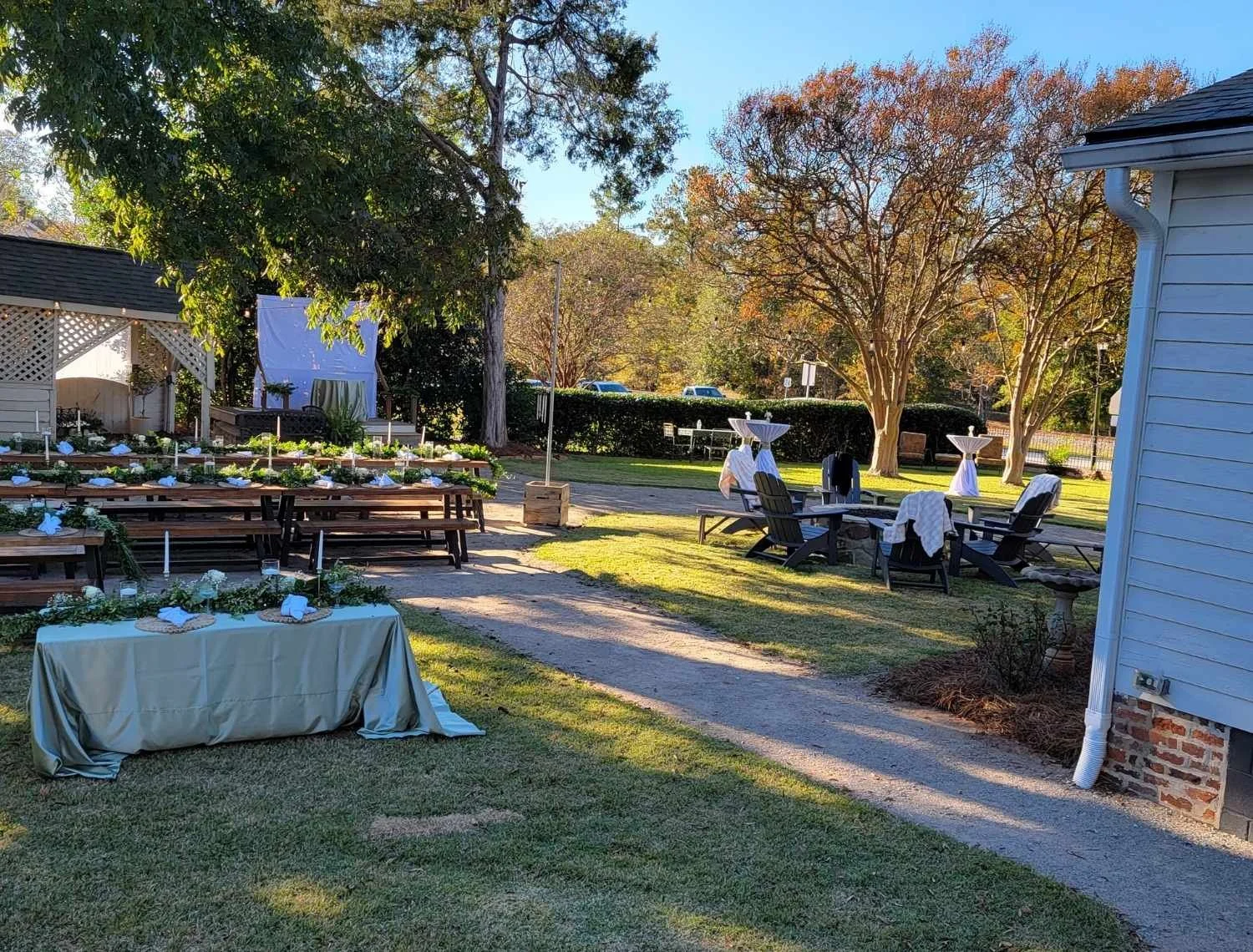 Reception tables with greenery and linens set up under trees at The Boland House pavilion