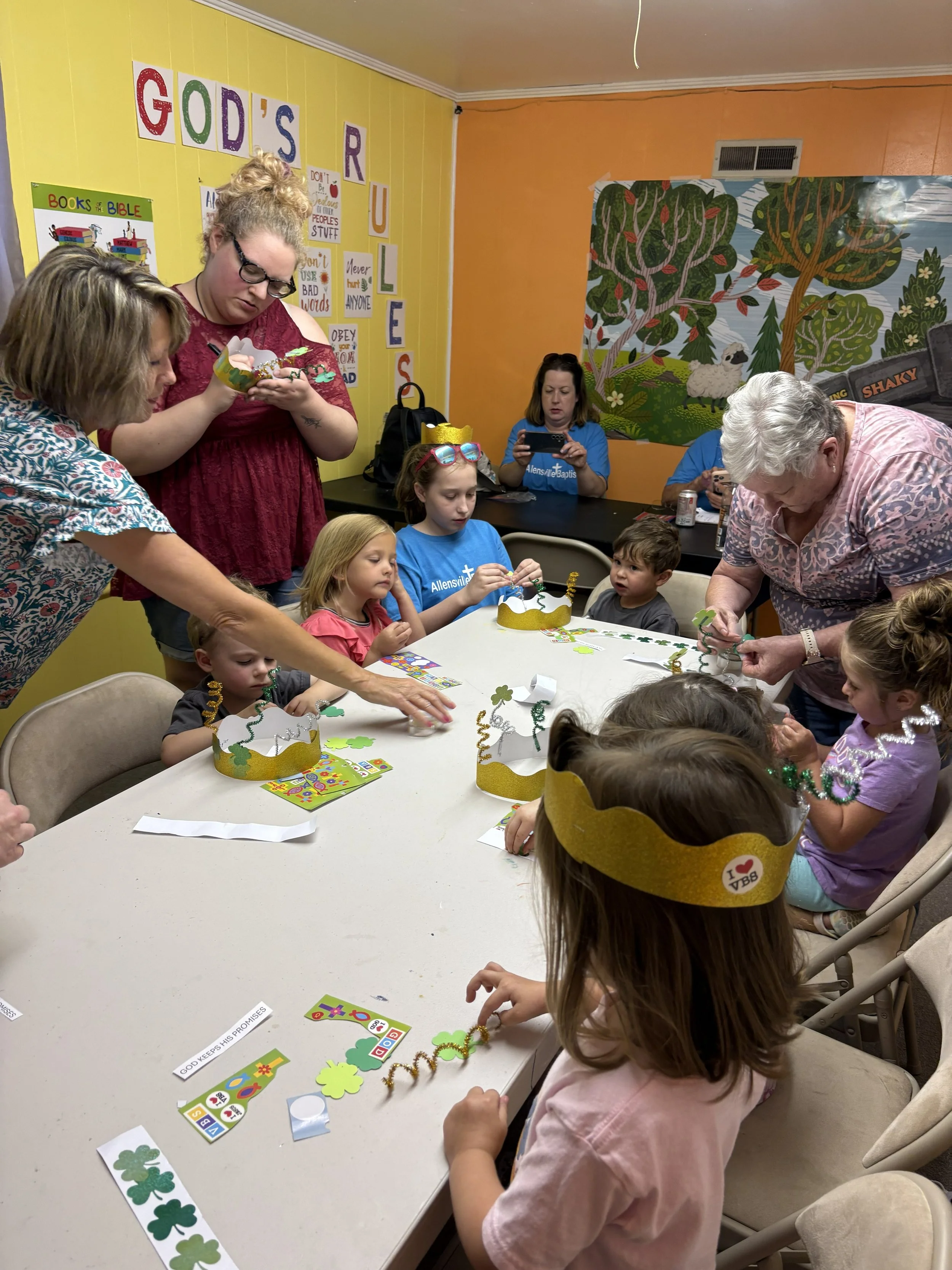 Children and adults gathered around a table participating in Vacation Bible School crafts.