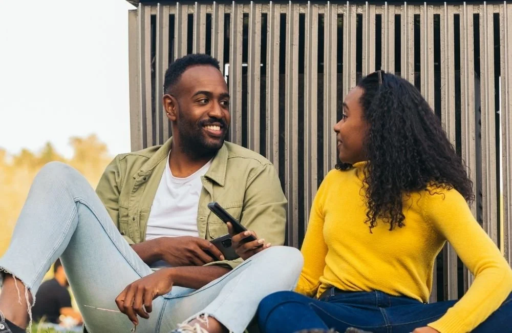 A couple sitting on the ground outside happy and talking
