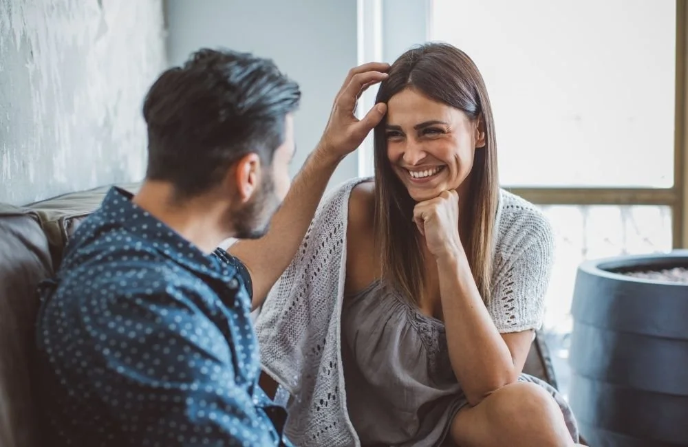A man reaching his hand out to touch the hair of his girlfriend while she smiles a him | Kathleen Killen Psychotherapy and Coaching