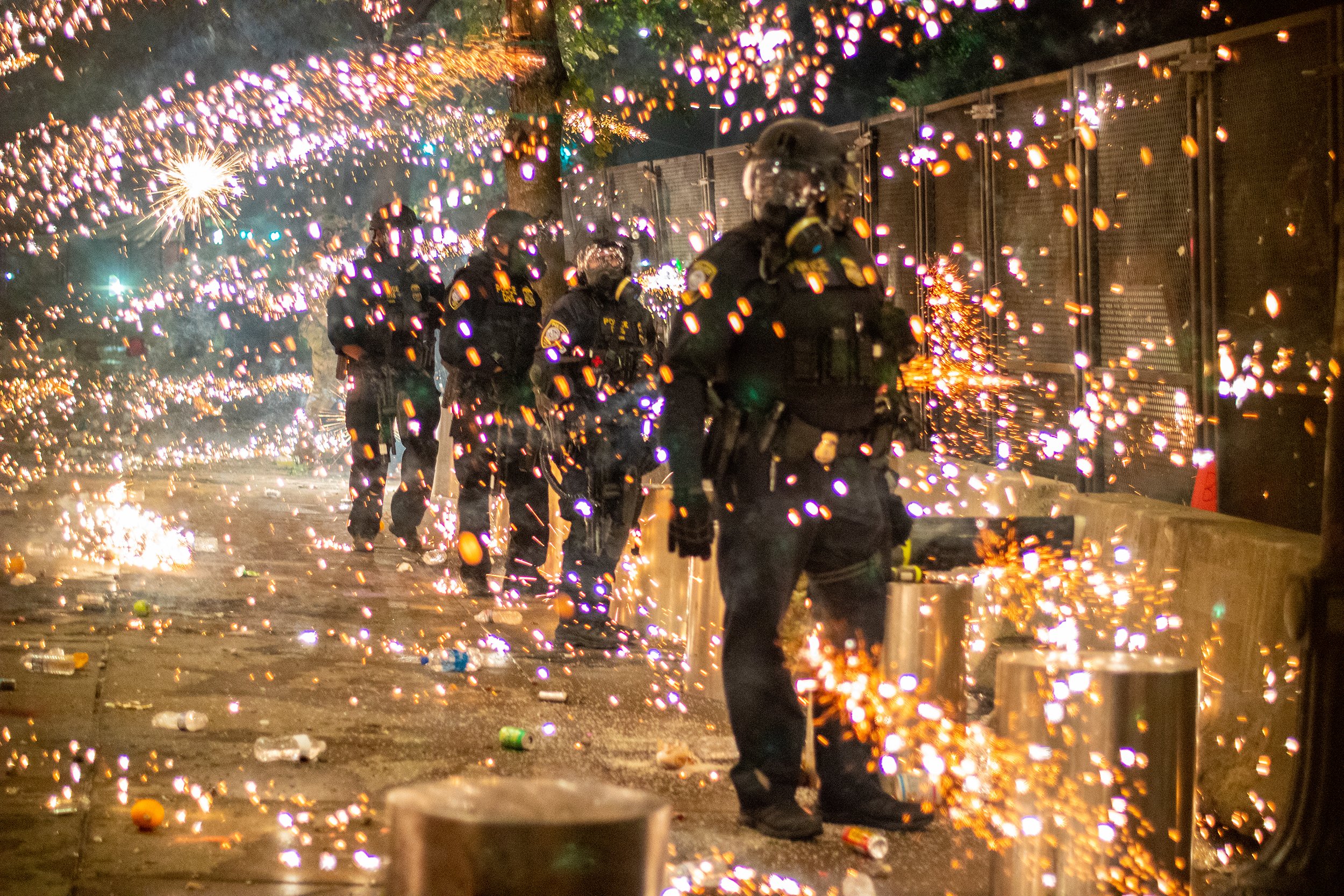 Artillery shell fireworks explode in flurry of sparks around unwavering police officers standing guard in front of the Multnomah County Justice Center during a Black Lives Matter protest July 24, 2020, in Portland, Ore. 