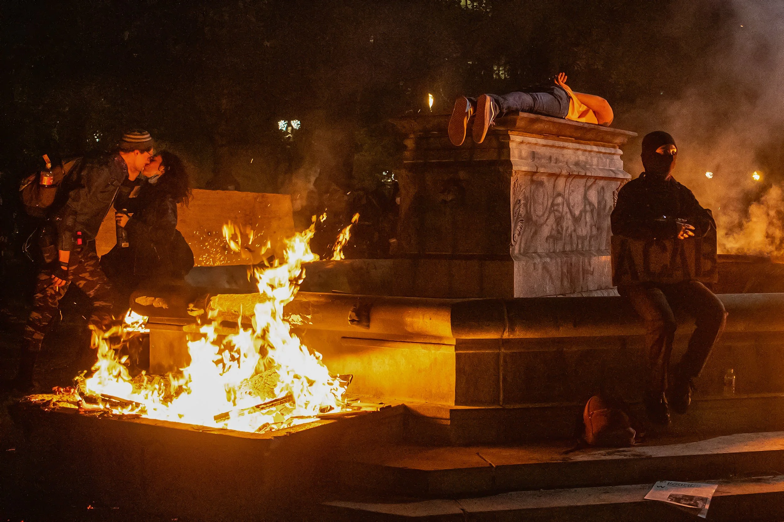 A unique mix of Black Lives Matter protesters gather by the flames near where the Elk Bronze statue once stood between Chapman and Lownsdale Squares on July 12, 2020, in downtown Portland, Ore.