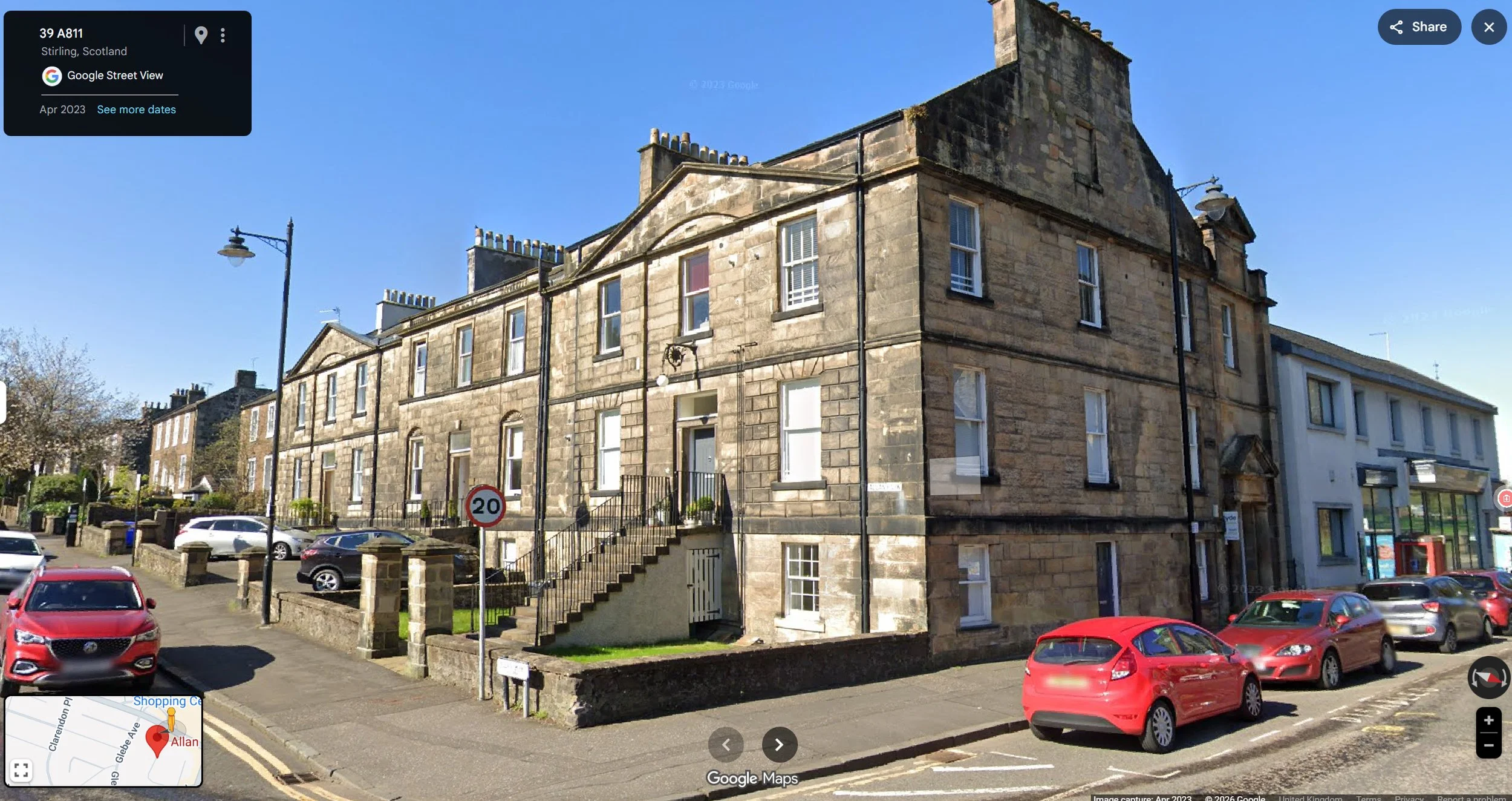 A historic stone apartment building on a street corner in Stirling, Scotland, with cars parked in front and a clear blue sky overhead.