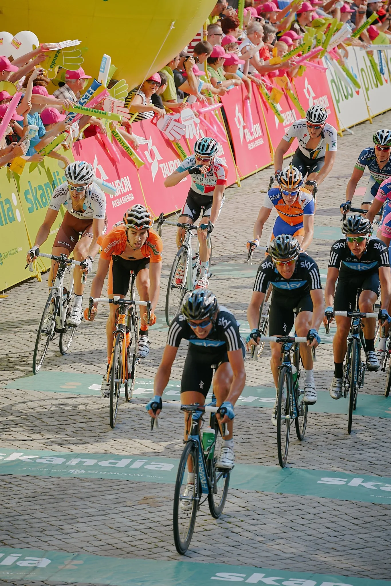 Cyclists compete in a race close to a crowd of spectators behind pink barriers during the event.