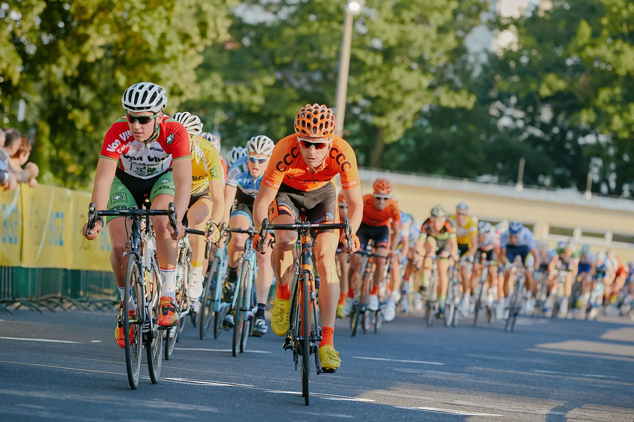 Cyclists competing in a race on a road, riding closely together with trees in the background.