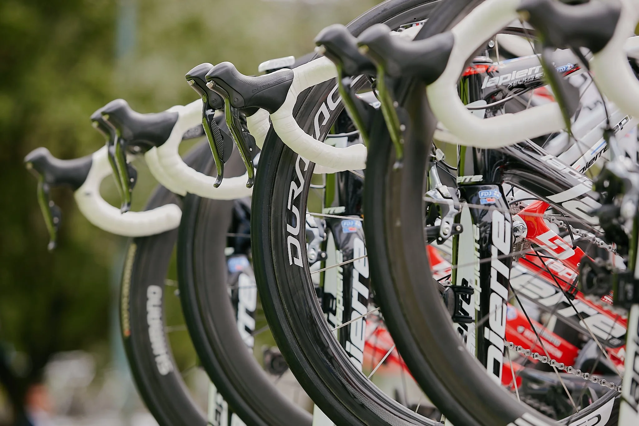 Multiple high-end road bicycles with white handlebars and black tires are lined up side by side outdoors.