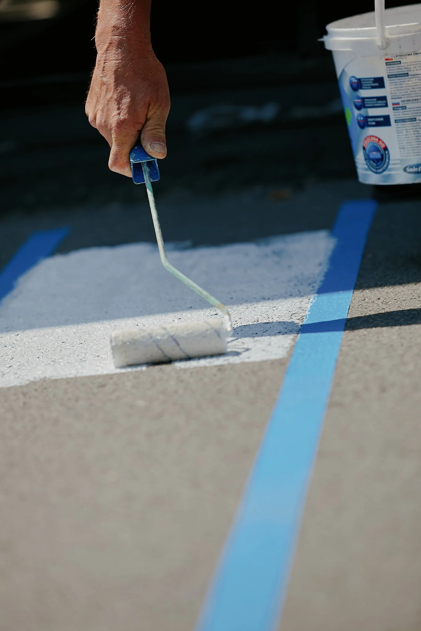 A person is using a paint roller to apply white paint on a surface marked with blue painter's tape.