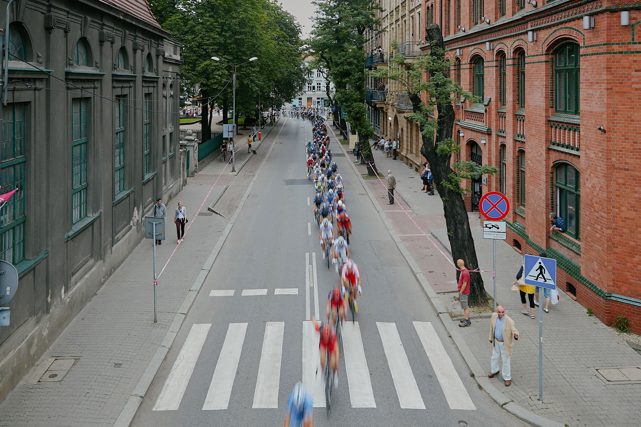 Cyclists participate in a race on a city street, with spectators and buildings lining the road.