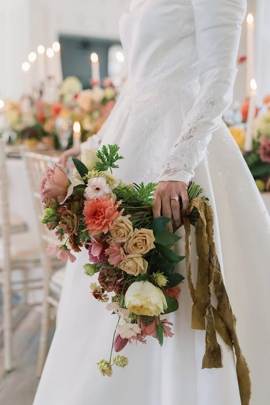 A bride holding a colorful bouquet of flowers in a wedding reception setting.