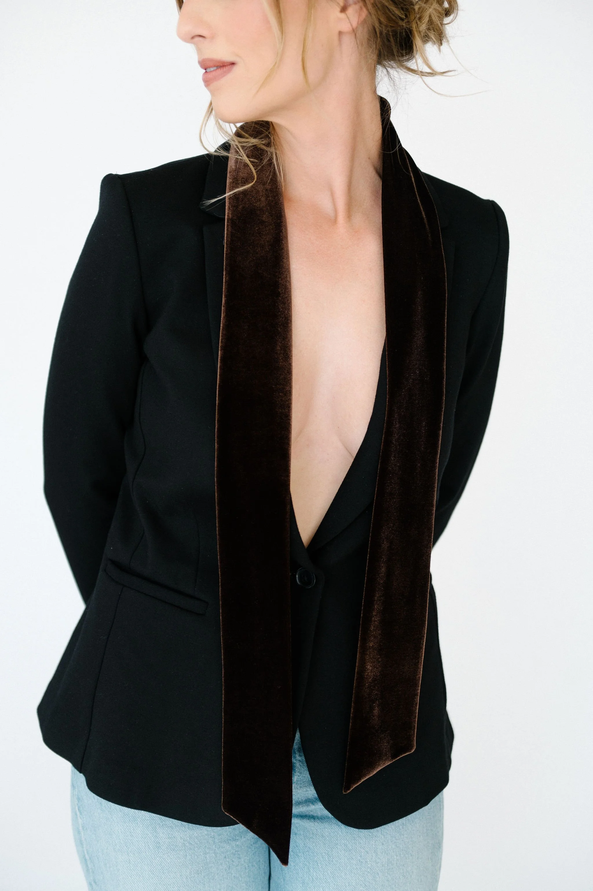 A woman with curly hair dressed in black, wearing a sheer black veil, standing on one foot in a ballet pose, against a white background.