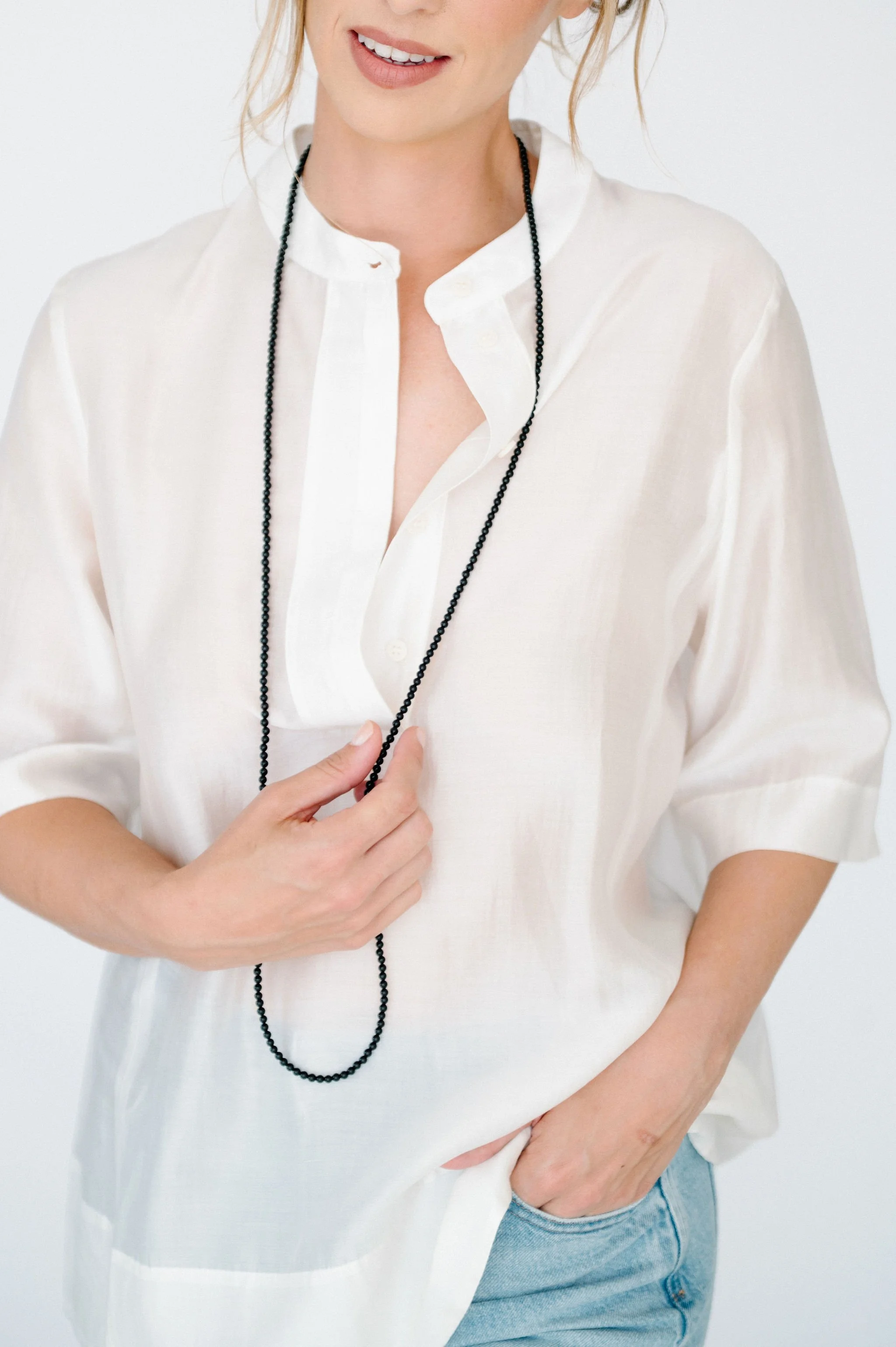 Woman in professional attire with a black blazer, white shirt, black shorts, and a brown black striped bow tie, standing against a plain white background.