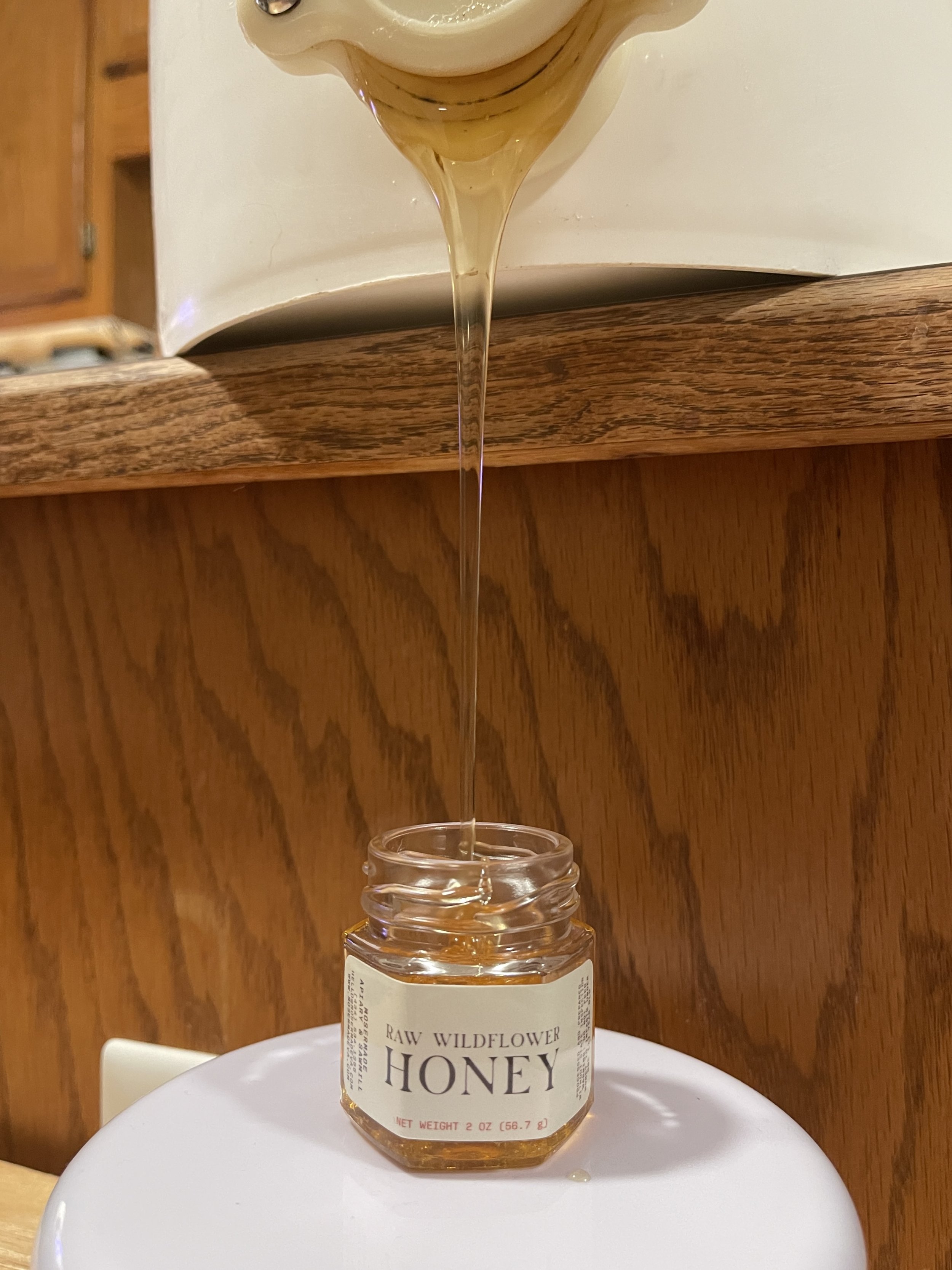 A bucket of raw wildflower honey is being poured into a Mosermade mini jar, highlighting the natural sweetness of raw honey.