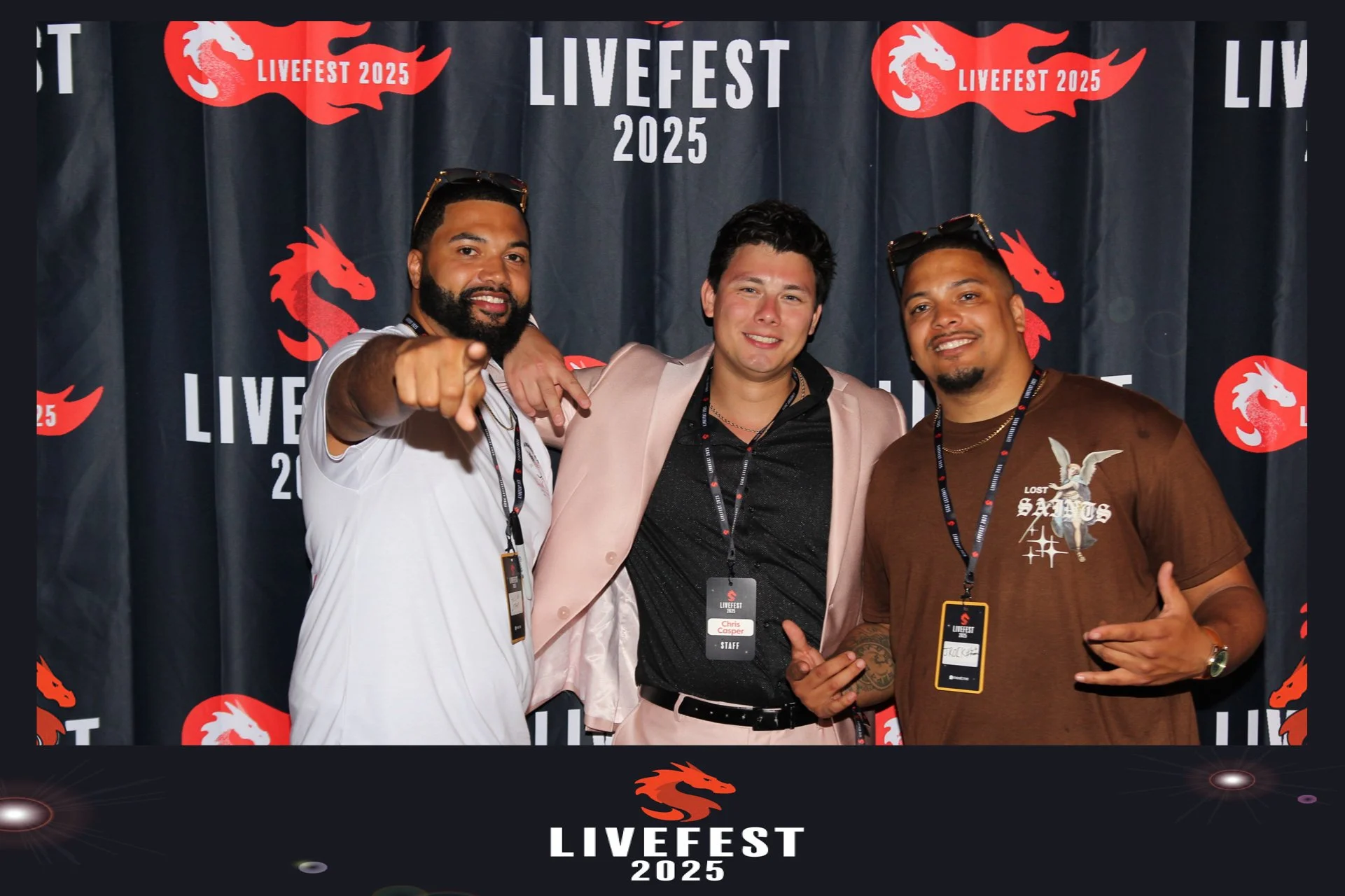 Three men standing together at LIVFEST 2025, posing for the photo. They are smiling and making hand gestures. The background features a dark curtain with red dragon logos and the text 'LIVFEST 2025'.