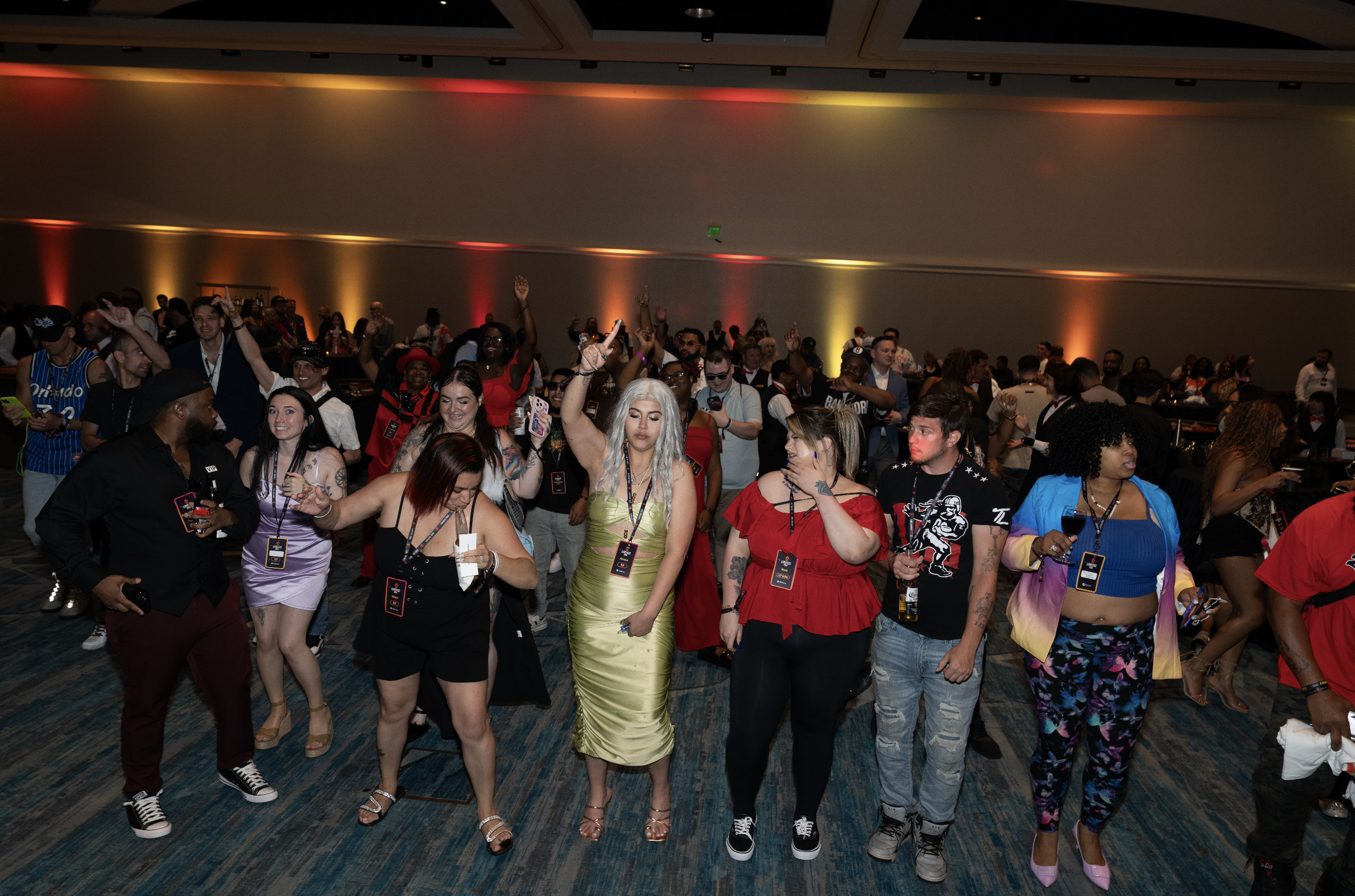 Crowd of diverse people dancing and enjoying themselves at a lively event or party with colorful lighting.