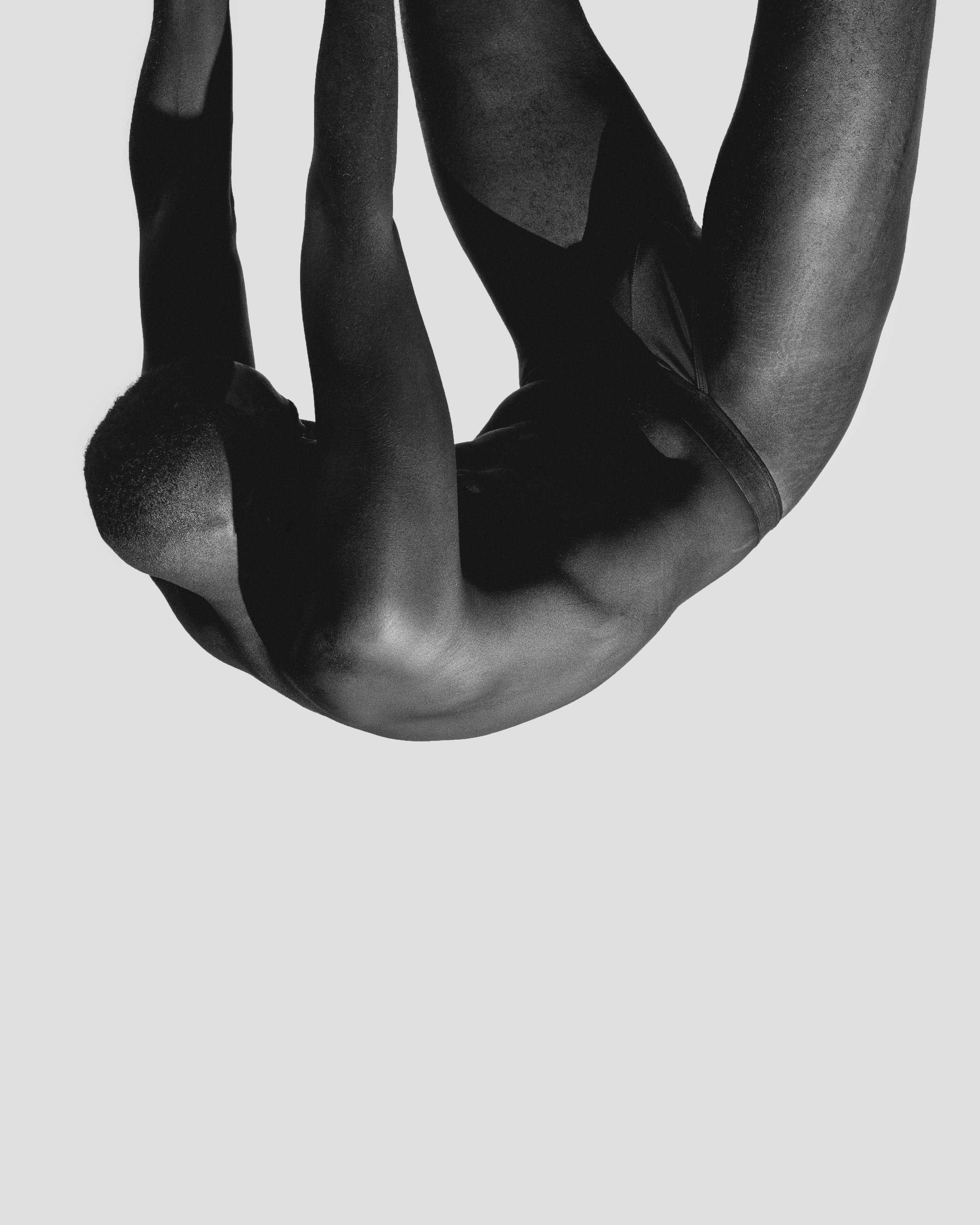 Black and white photo of a person in a yoga pose, with their body bent backward and supported by their arms, against a light background.