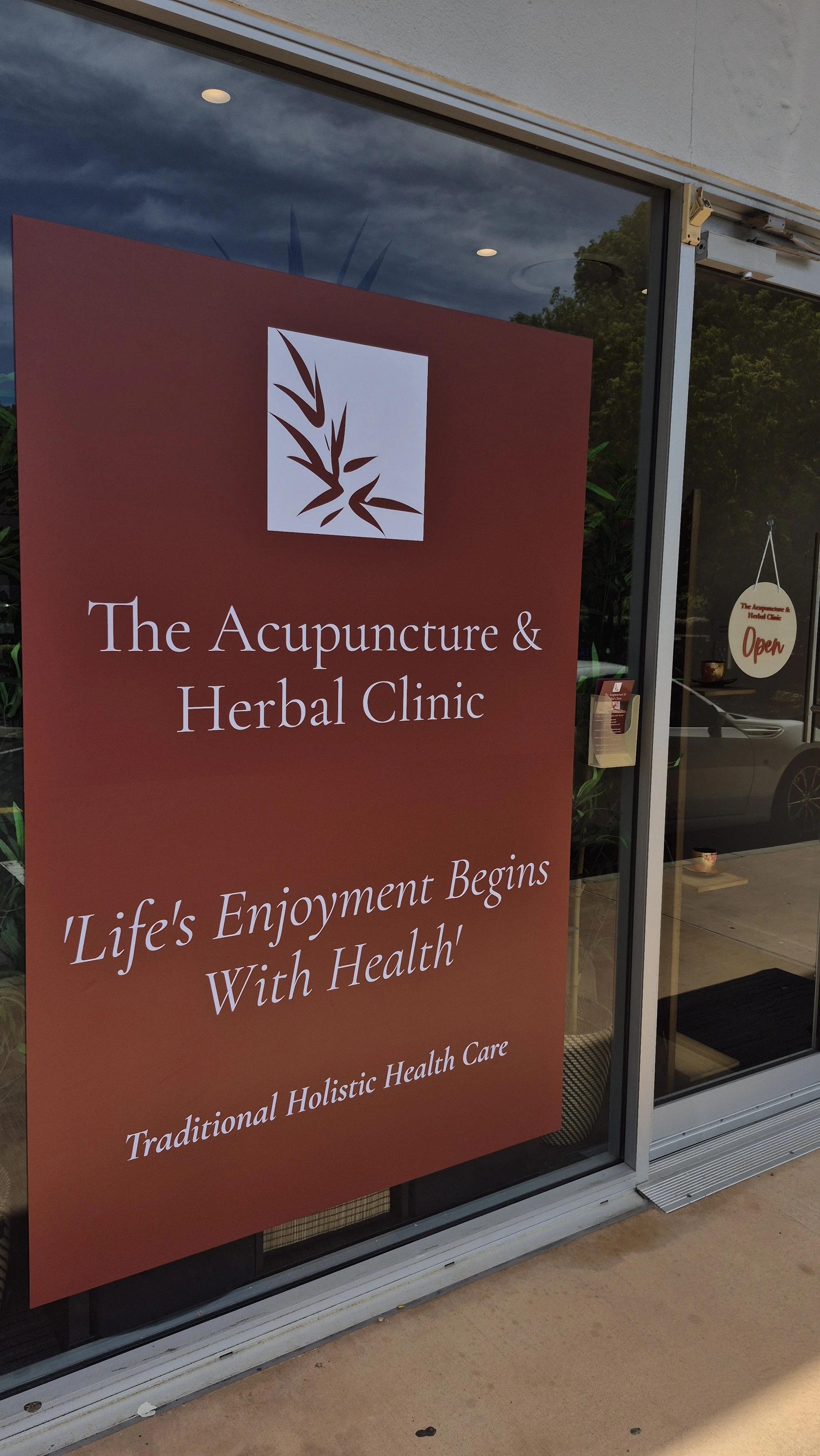 Sign outside the acupuncture and herbal clinic with a logo, the clinic's name, and the slogan 'Life's Enjoyment Begins With Health'.