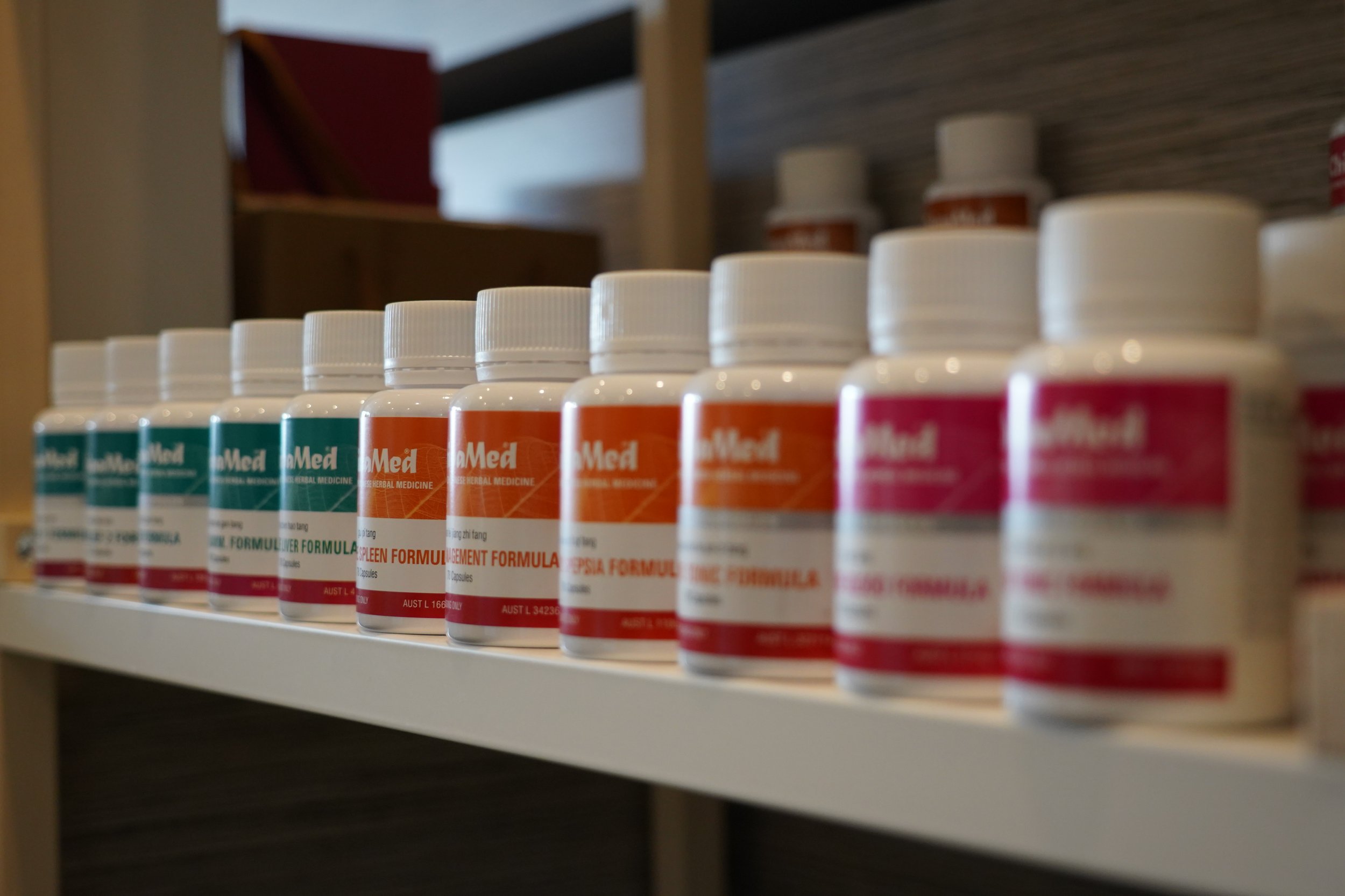 A white container tipped over with beige capsules spilling out, with green foliage in the background.