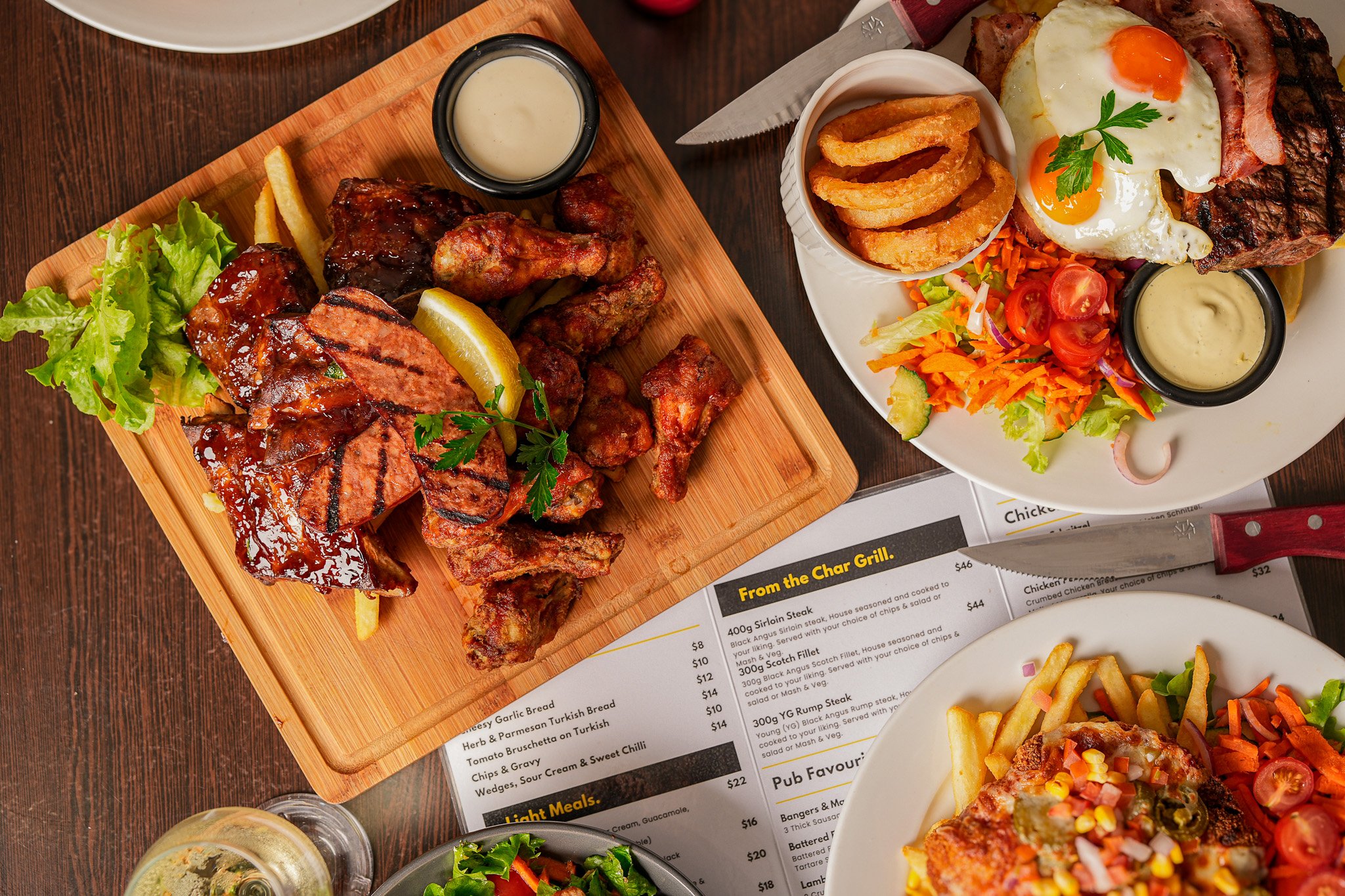 Plates of grilled meats with French fries, salad, and dipping sauces on a wooden table.