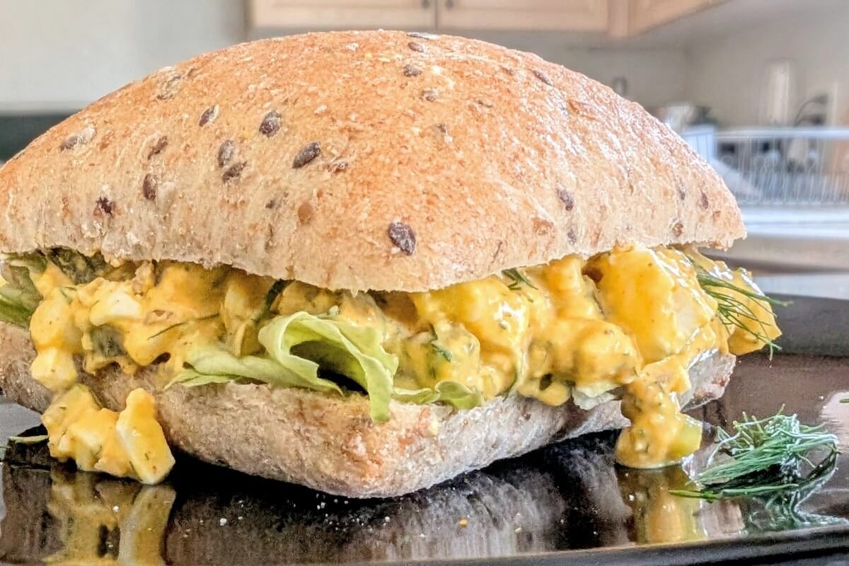 Close-up of a no mayo egg salad sandwich recipe on whole grain bread with lettuce and fresh dill, served on a black plate