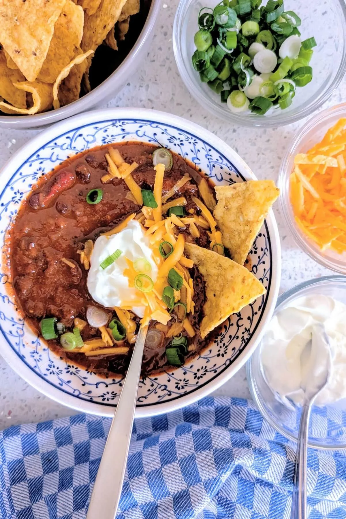Bowl of chunky beef chili with black beans, cheddar cheese, sour cream, and fresh scallions, served with tortilla chips