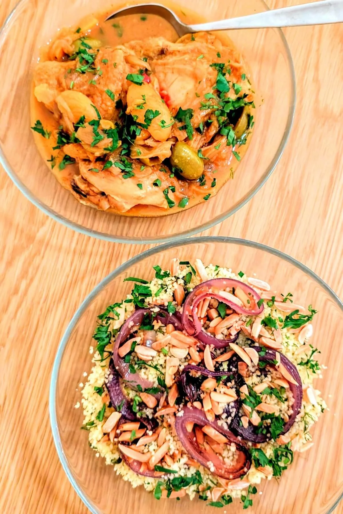 Bowl of kettle couscous topped with onions, herbs, preserved lemon vinaigrette, and almonds beside a bowl of chicken tagine