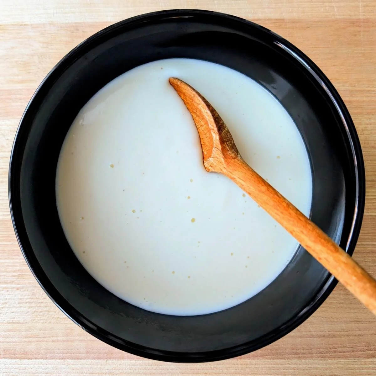 Spoon resting in basic bechamel sauce in a bowl on a wooden countertop