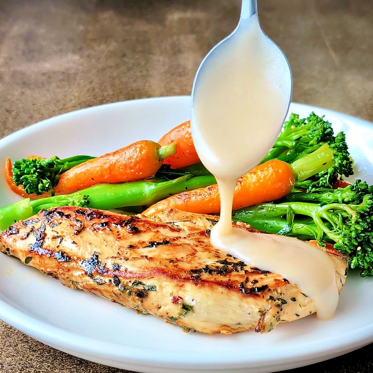 Spooning velouté sauce over cooked chicken on a plate with vegetables