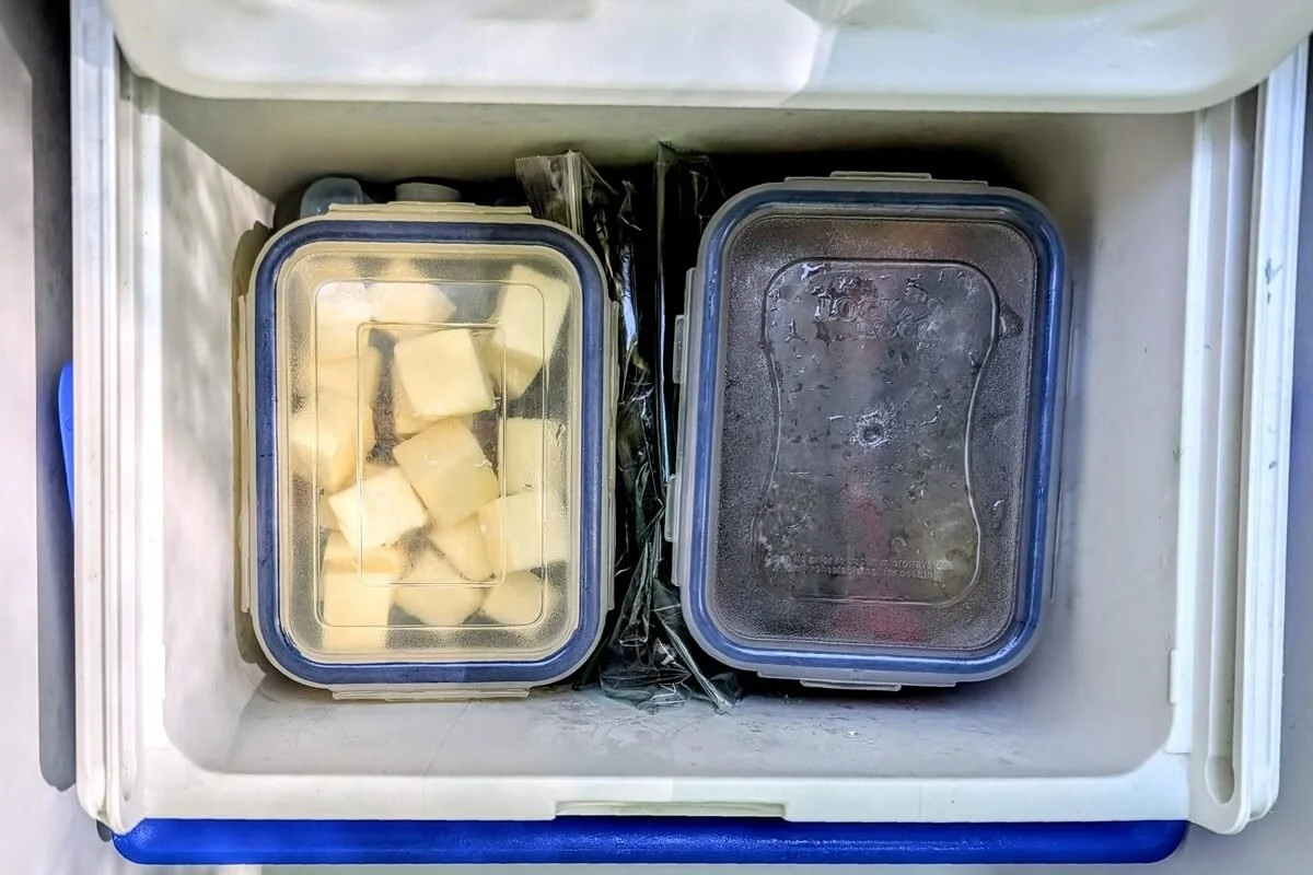Small cooler placed inside a large cooler, holding pickles, butter, and herbs in locking containers