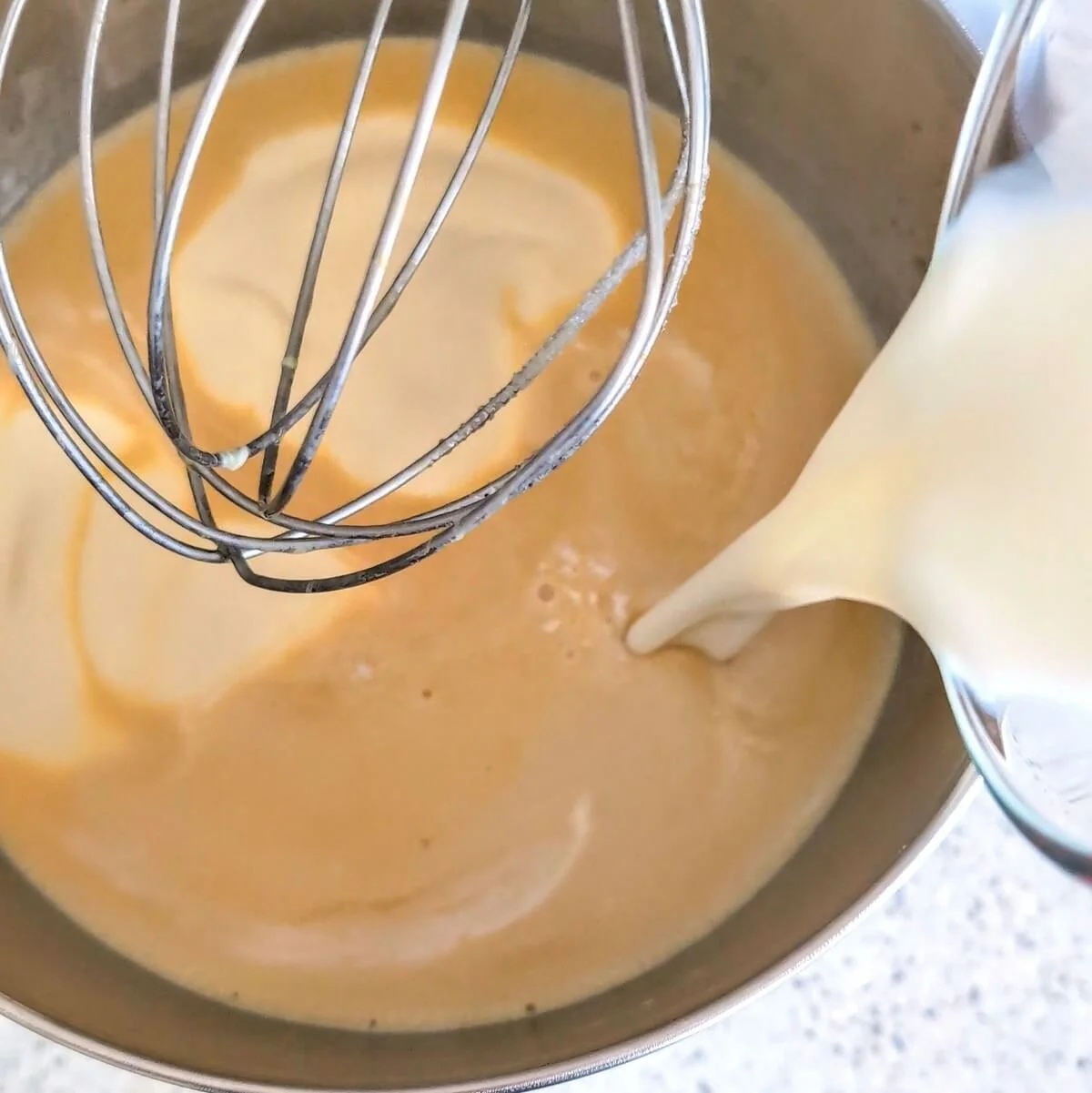 Pouring milk and cream into the eggnog base for a rich homemade eggnog recipe
