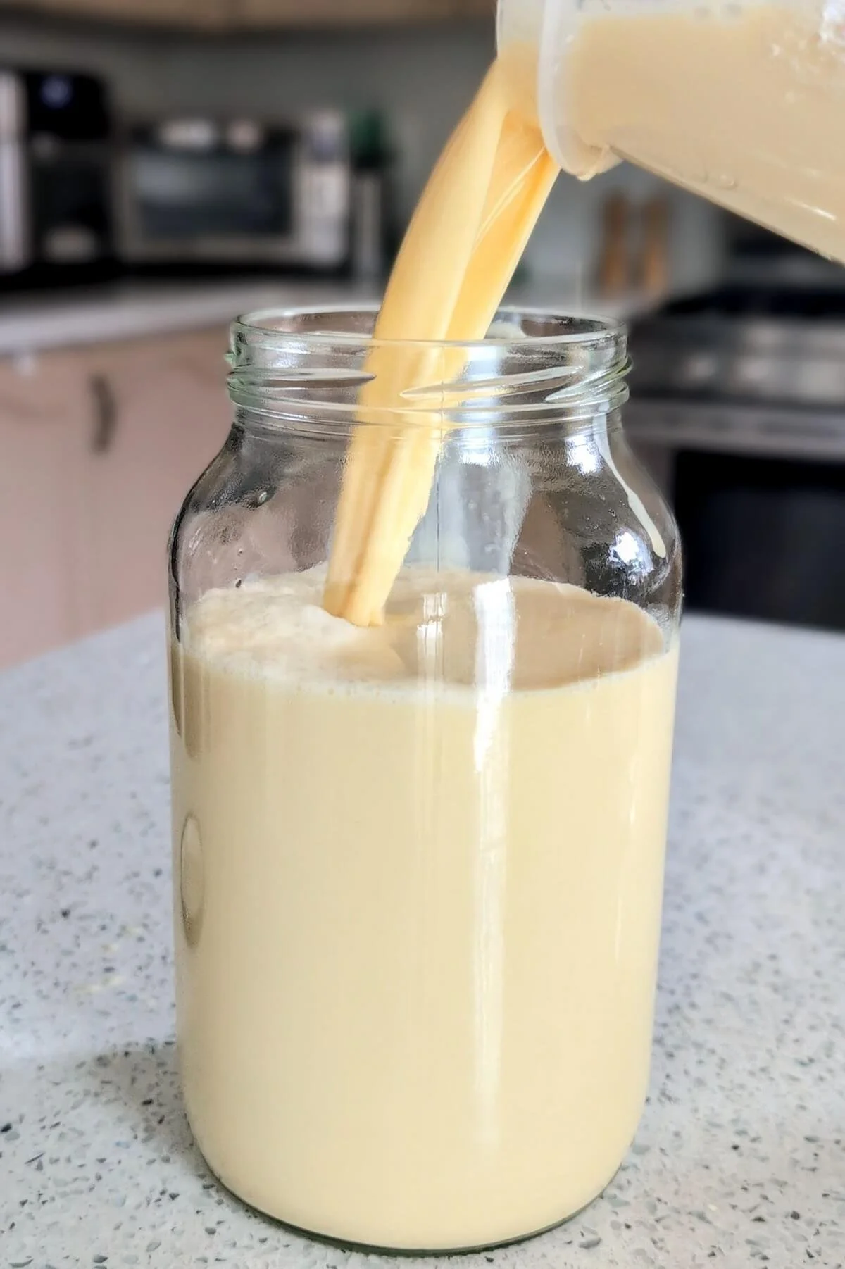 Smooth eggnog mixture being poured into glass jars for aging