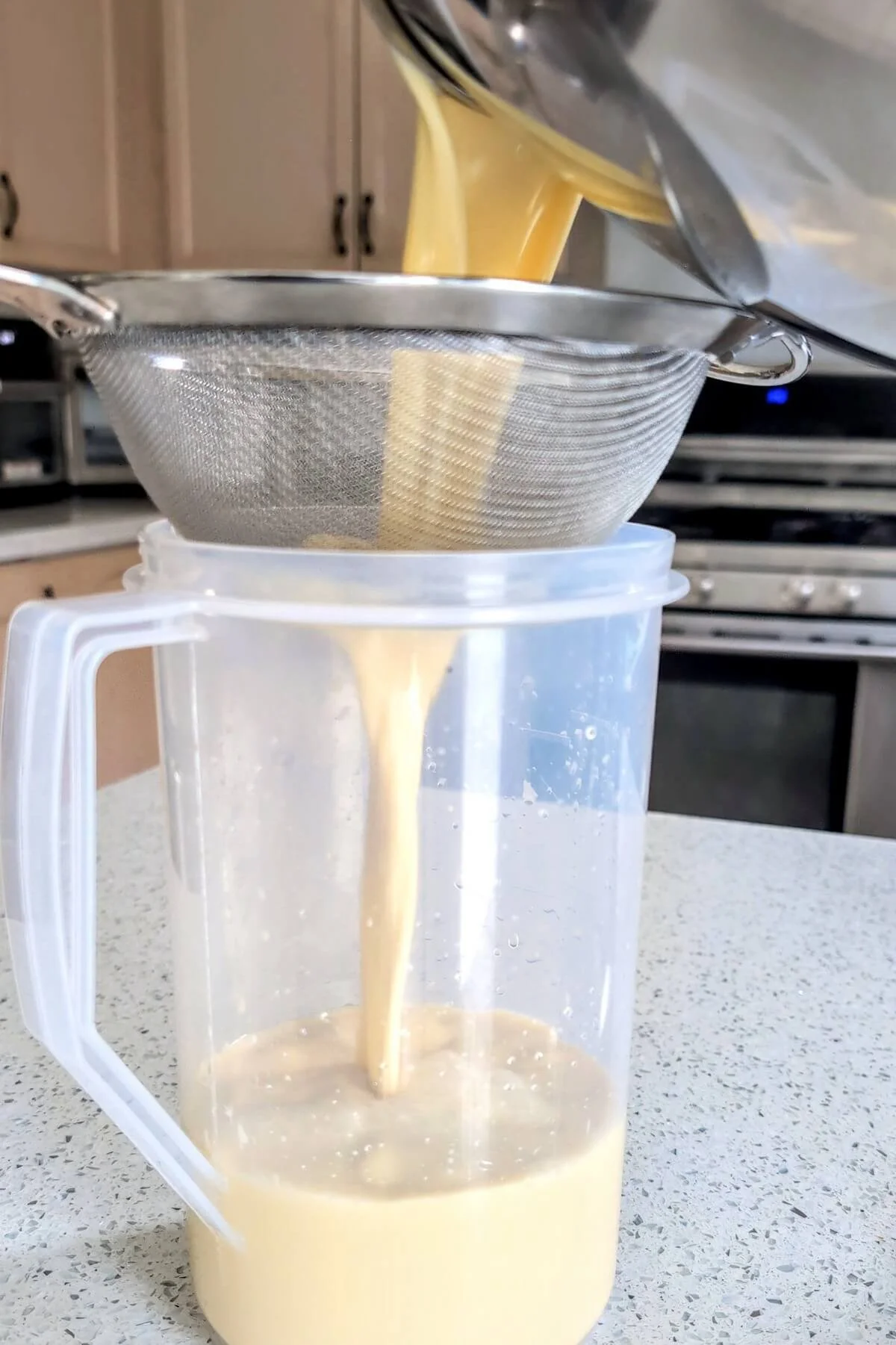 Straining homemade eggnog through a fine mesh sieve into a pitcher