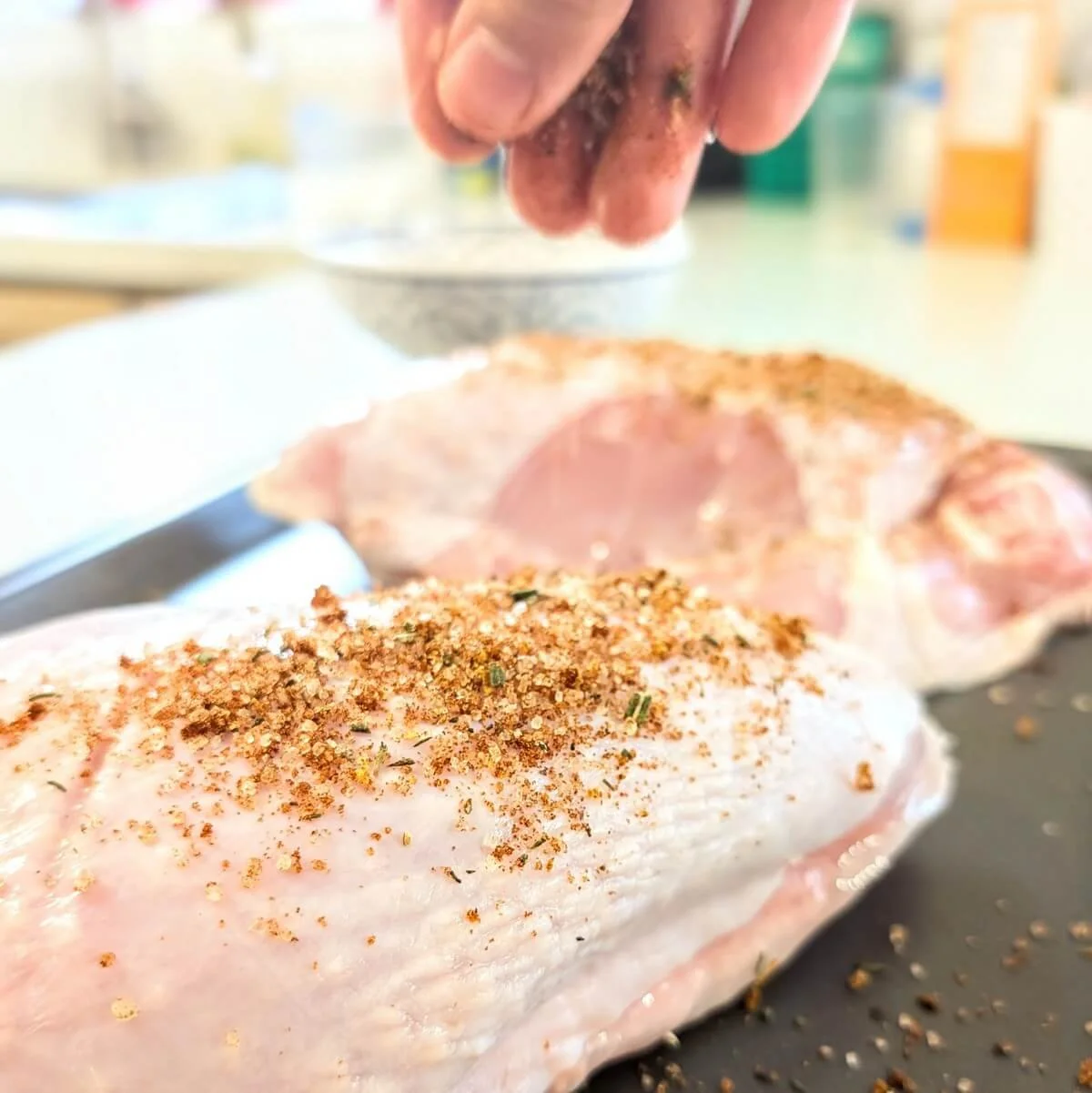 Sprinkling dry brine over skin-on turkey breasts on a tray
