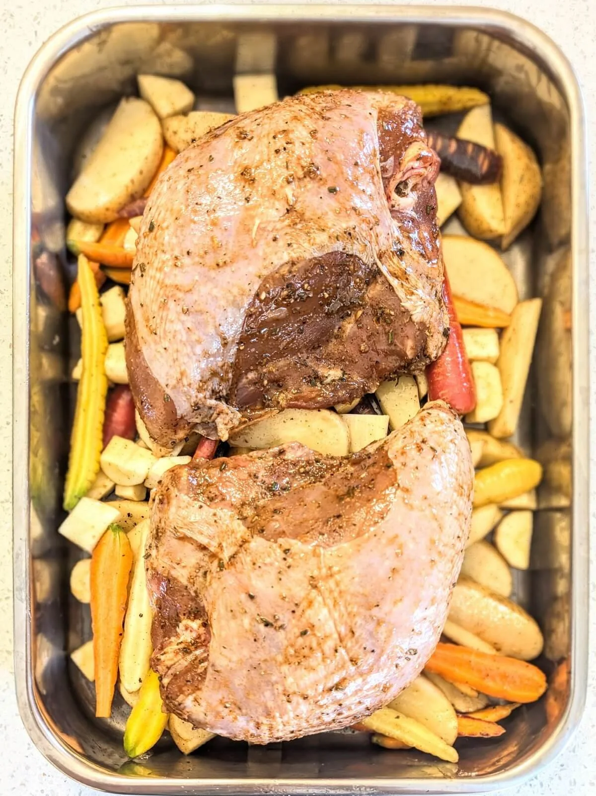 Dry-brined turkey breasts placed on top of seasoned root veggies in a pan