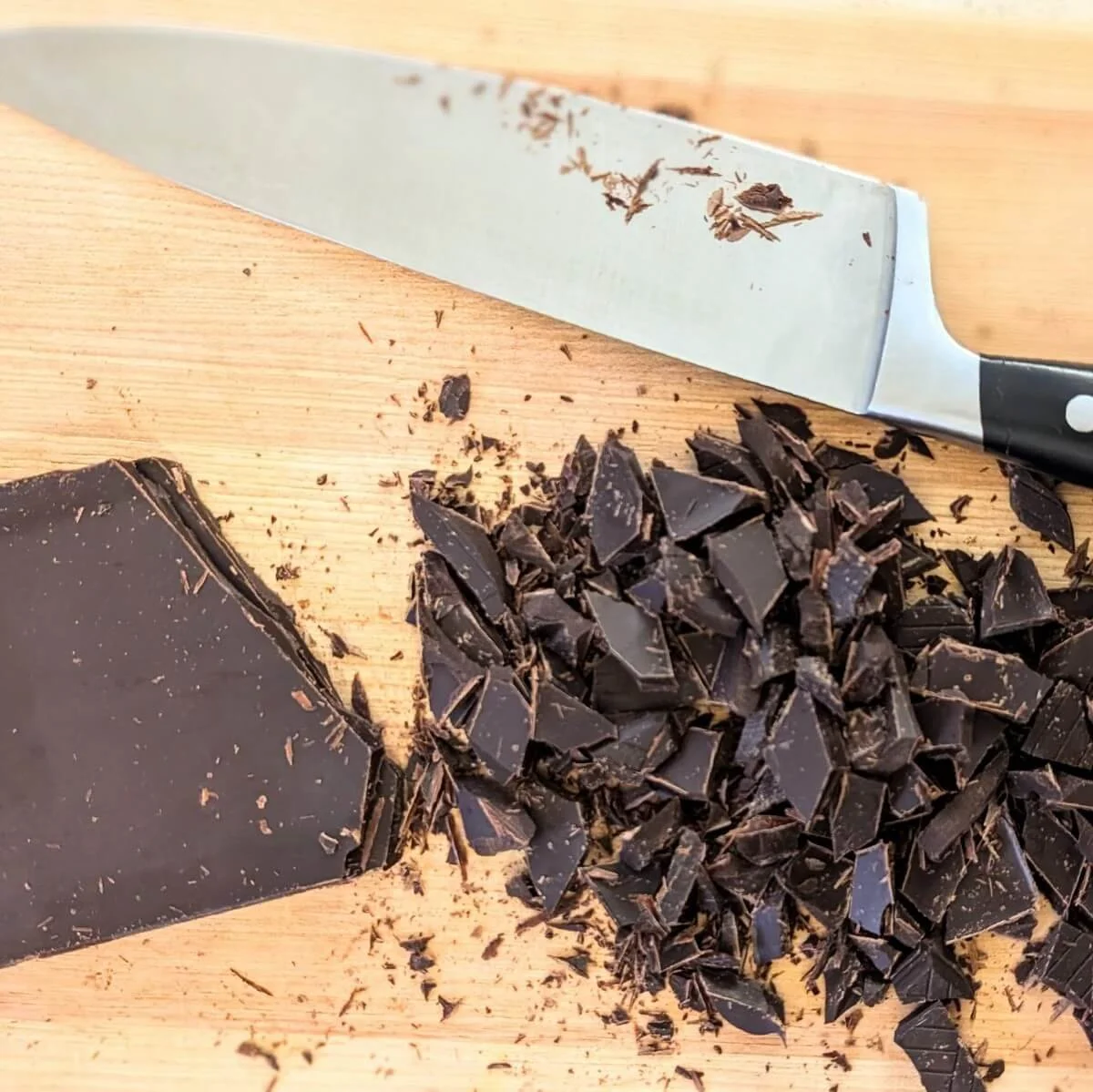 Chopped dark chocolate chunks on a cutting board with a knife for dark chocolate sea salt cookies