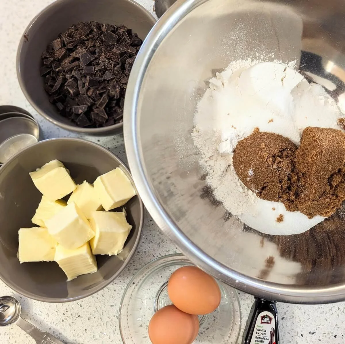 Baking ingredients for salted chocolate chunk cookies, arranged in small bowls on a white countertop