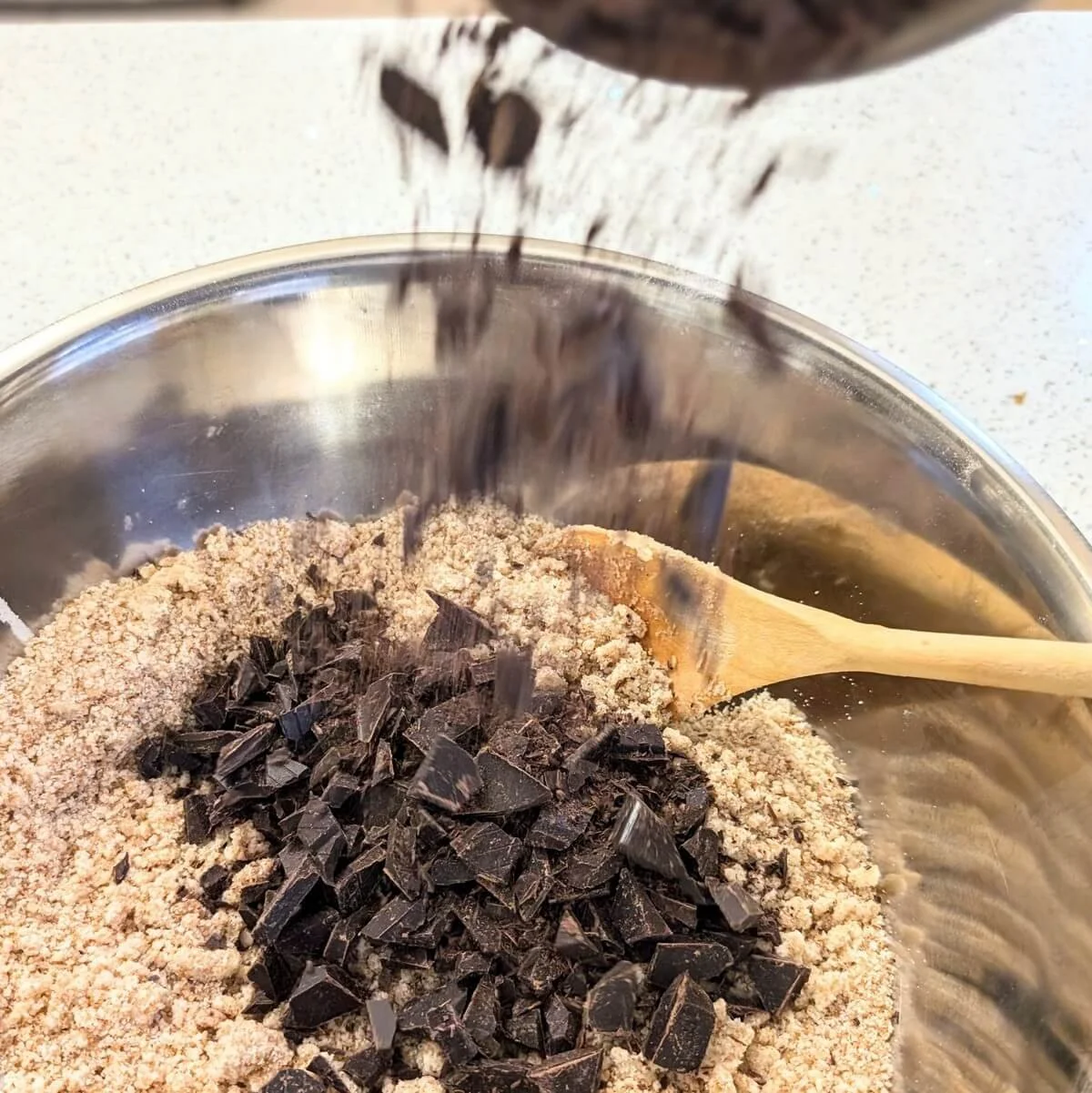 Adding dark chocolate chunks to the bowl for dark chocolate chunk cookie recipe