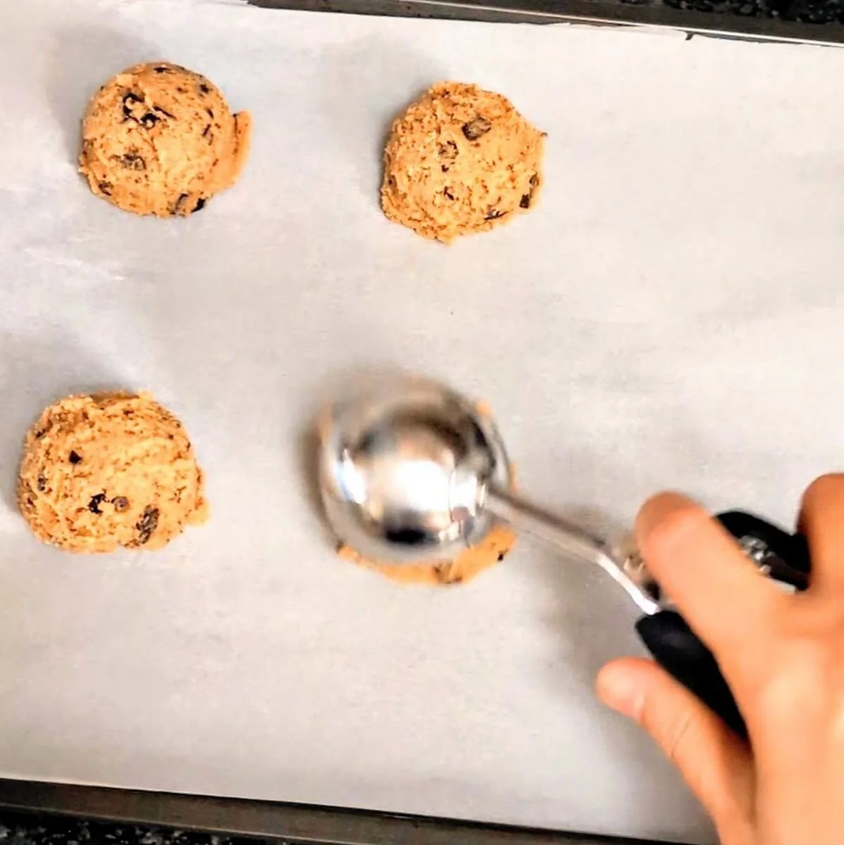 Overhead view of chocolate chunk cookie dough being scooped on a parchment-lined baking sheet
