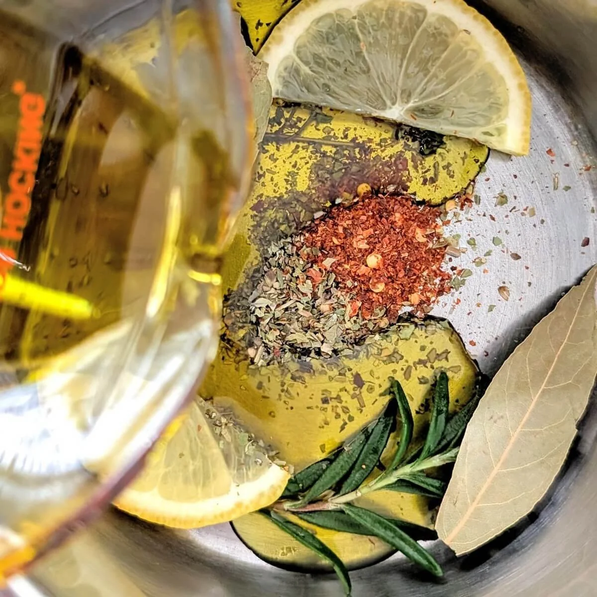Olive oil and red wine vinegar being poured into a saucepan with herbs and spices for antipasto marinade