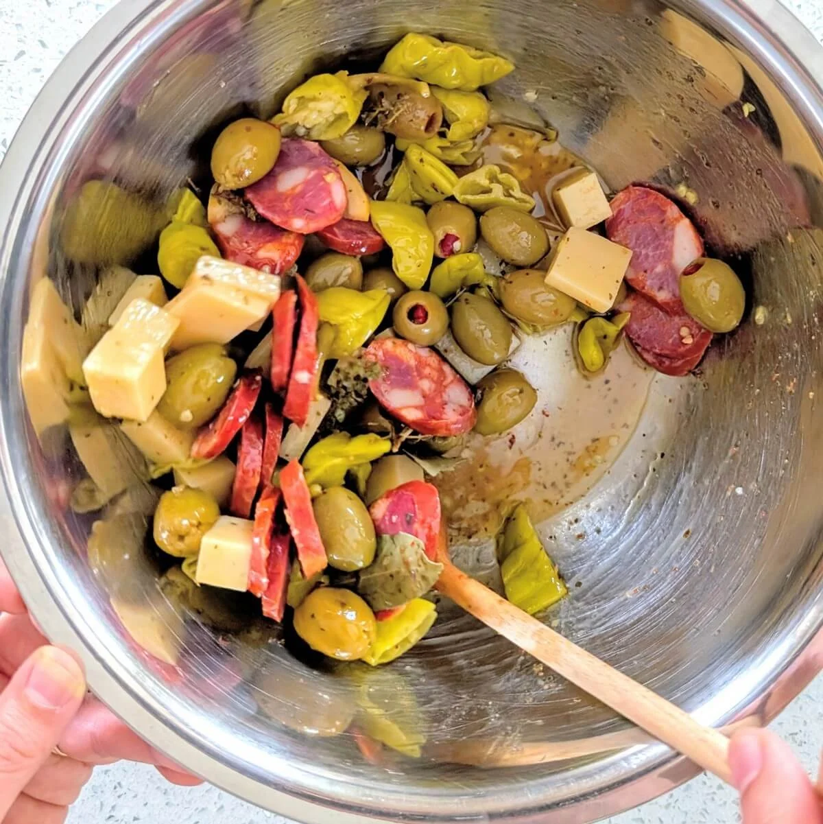 Antipasto olives meat cheese and pickles being stirred in a bowl with homemade olive oil and vinegar marinade