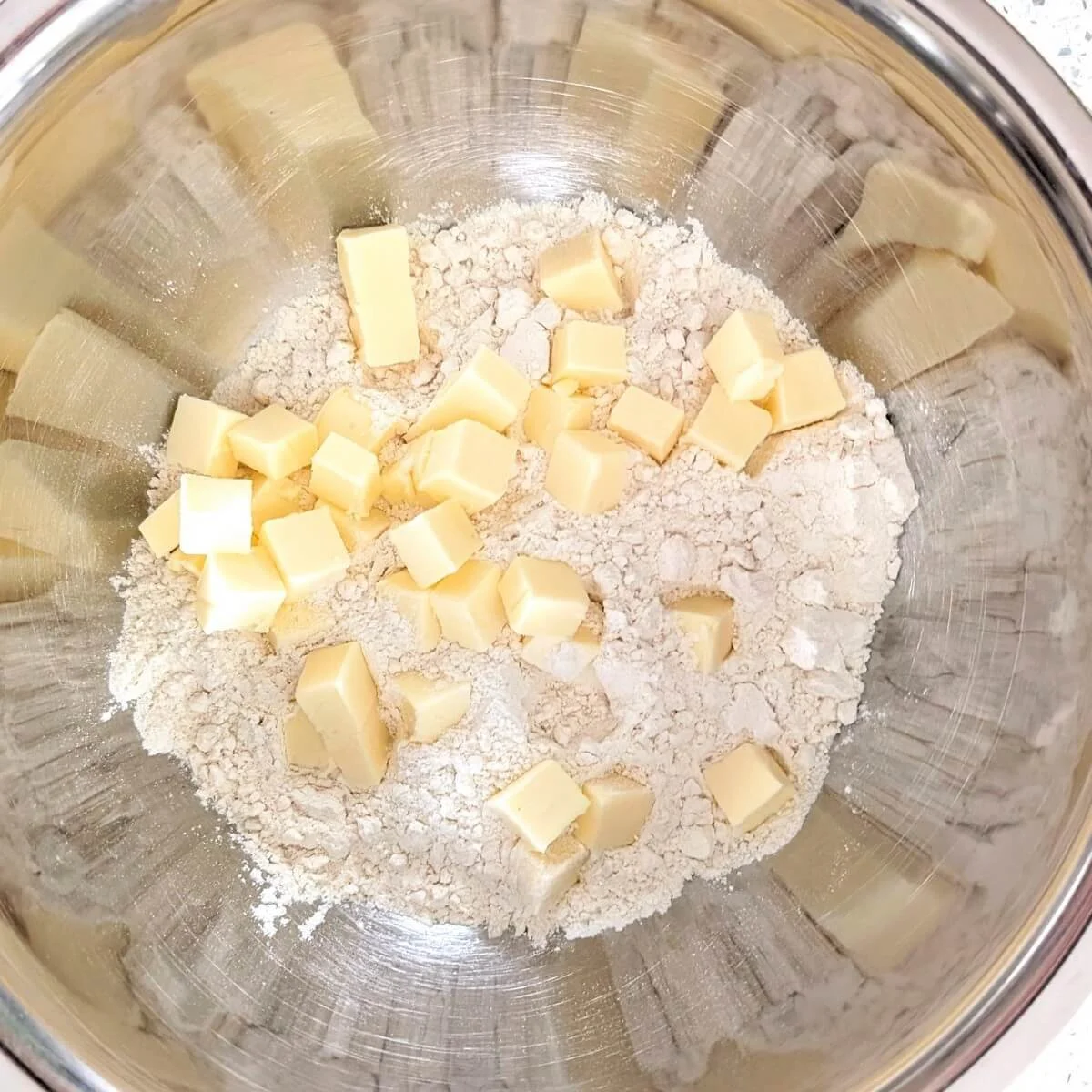 Measured flour in a mixing bowl with cubes of butter to make a homemade pie crust from scratch