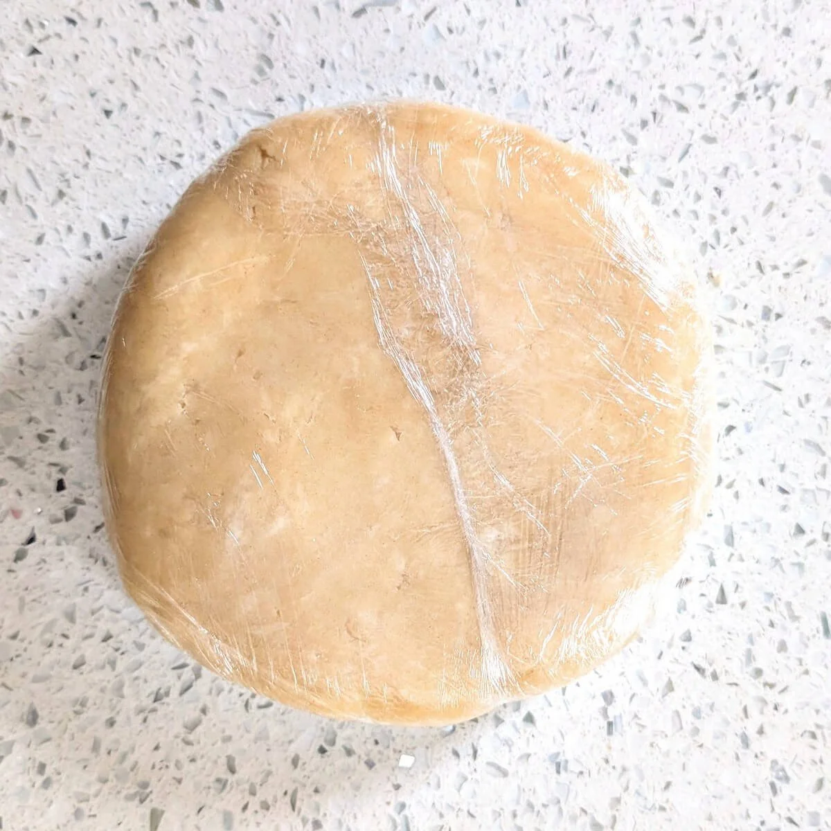 Plastic-wrapped pie dough disk on a countertop to make pumpkin pie crust