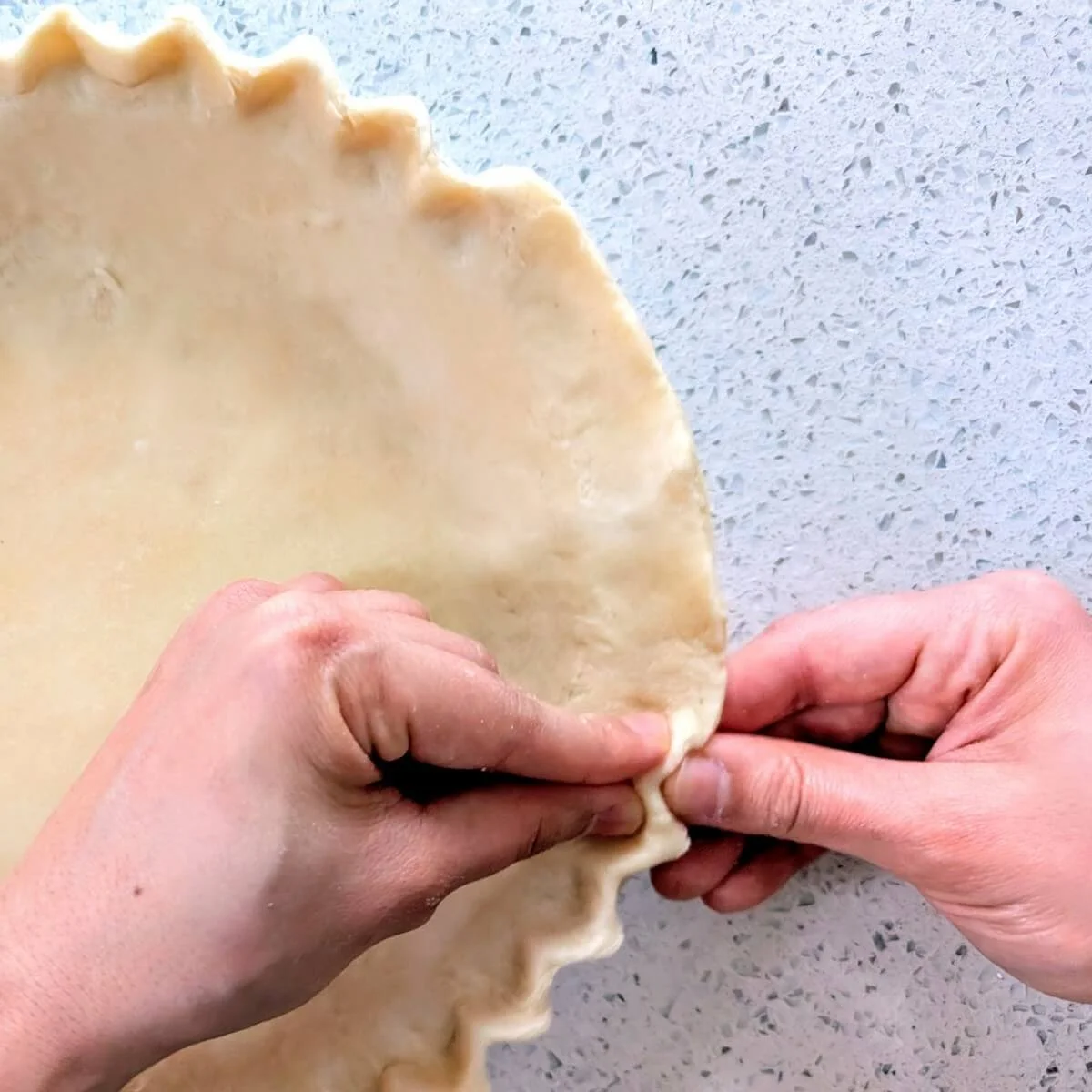 Shaping the crimped edge of the pie dough in a pie pan using thumbs and fingers