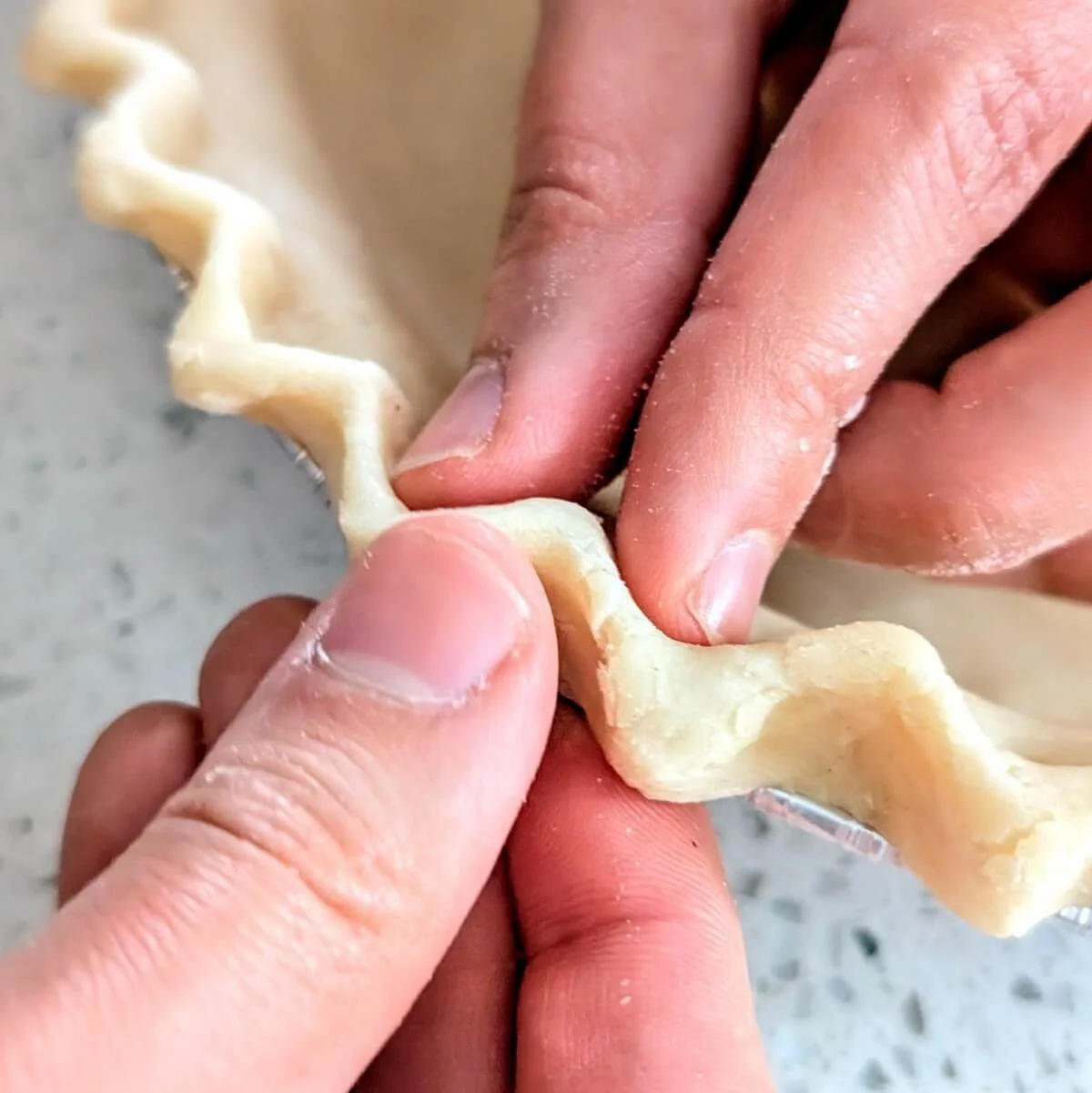 Close-up of thumb and fingers crimping the edge of a homemade pie crust for pumpkin pie