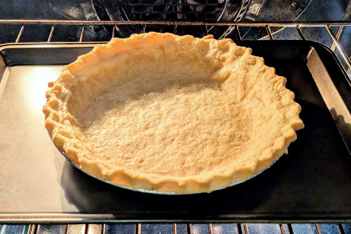 Blind-baking a pumpkin pie crust with weights removed to fully bake the bottom of the crust