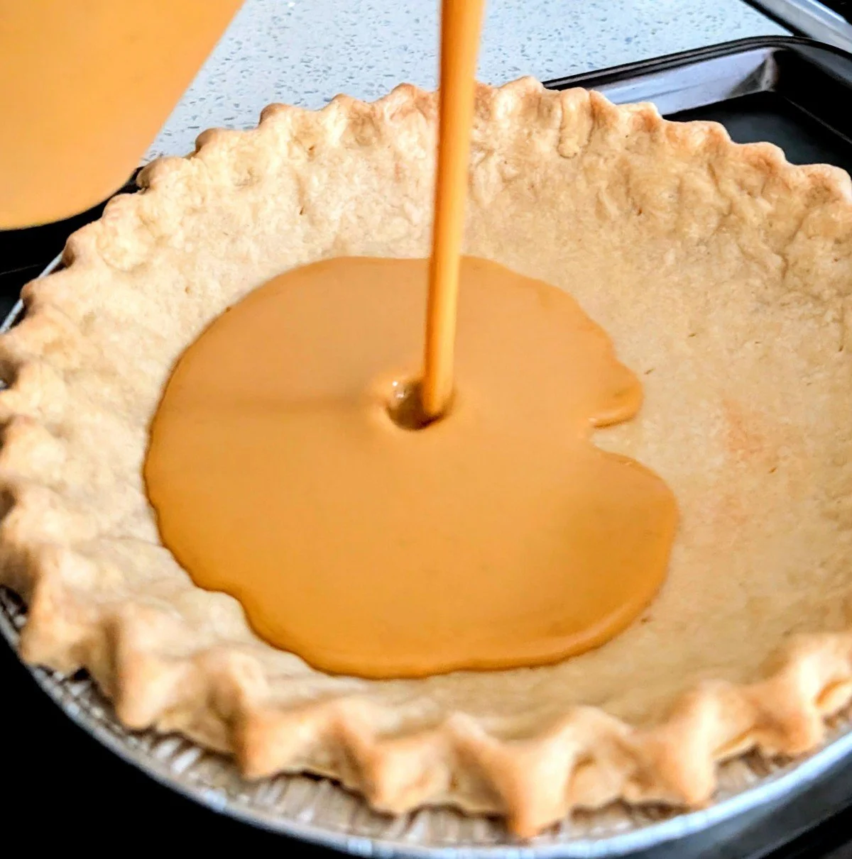 Pumpkin pie filling being poured into a blind-baked homemade pie crust