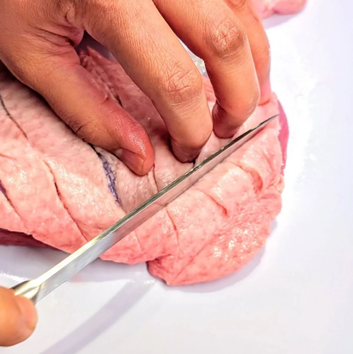 Close up of duck breast skin being scored for even fat rendering