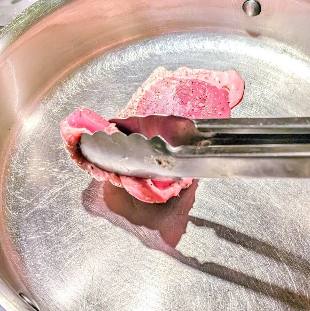 Placing scored duck breast skin-side down in cold stainless steel pan for searing